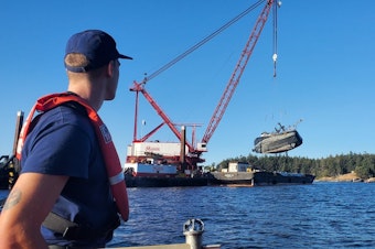 caption: A Coast Guard member watches the Aleutian Isle being lifted onto a barge off San Juan Island on Sept. 21.