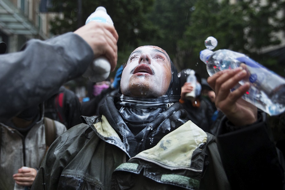 caption: A protester has milk and water poured into their eyes after tear gas was deployed by Seattle police officers on Saturday, May 30, 2020, near Westlake Park in Seattle. Thousands gathered in protest following the murder of George Floyd, beginning daily protests that would last for several months in Seattle.