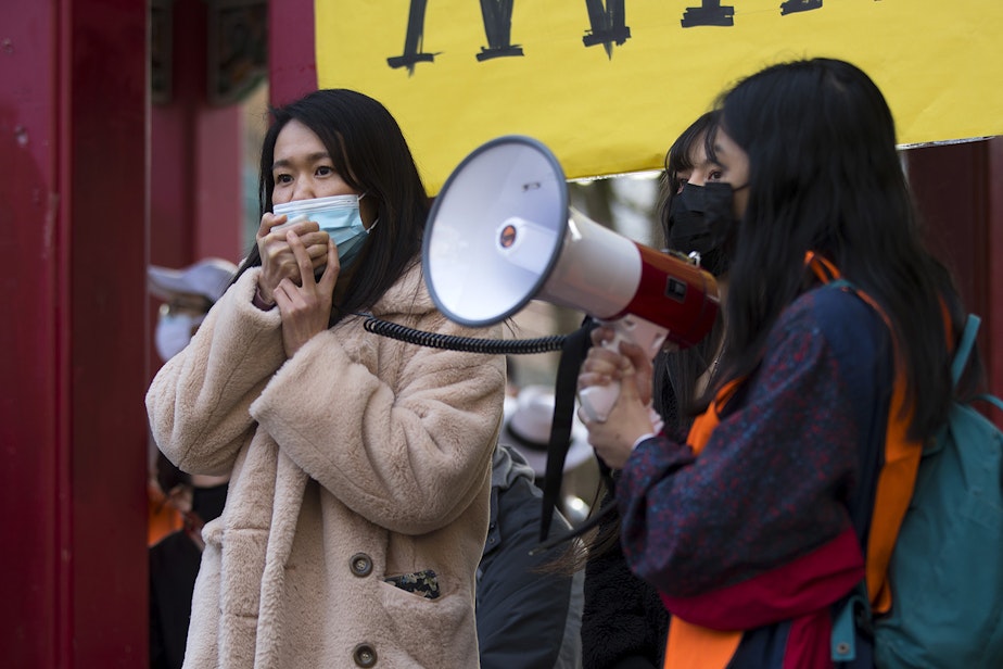 caption: Noriko Nasu, left, speaks to the crowd during the ‘We Are Not Silent’ rally against anti-Asian hate and bias on March 13, 2021 at Hing Hay Park in Seattle. Nasu was  attacked last month in the Chinatown International-District. Several days of actions are planned by rally organizers in the Seattle area following recent attacks and violence against Asian Americans and Pacific Islanders.