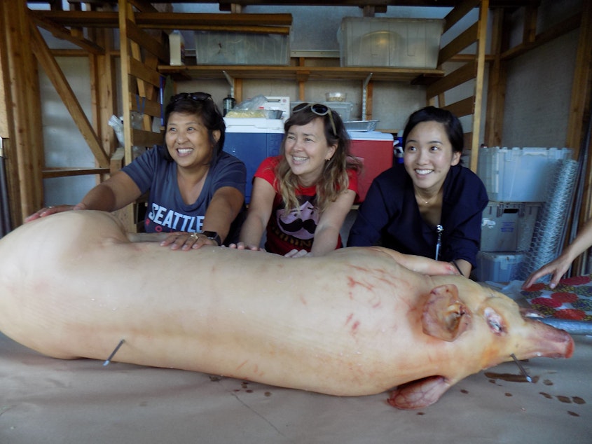 caption: Left to right: Mai Nguyen, Anne Xuan Clark, and Tiffany Wong sew up the pig's belly after stuffing it with garlic, lemongrass and other aromatics.