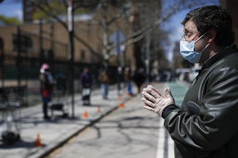 caption: Christopher Love, general manager of the Covenant Mercy Mission, leads a prayer beside a line of visitors waiting for food donations at Manor Community Church on Saturday in New York. An additional 758 people died from the coronavirus over the past 24 hours, Gov. Andrew Cuomo said on Sunday.