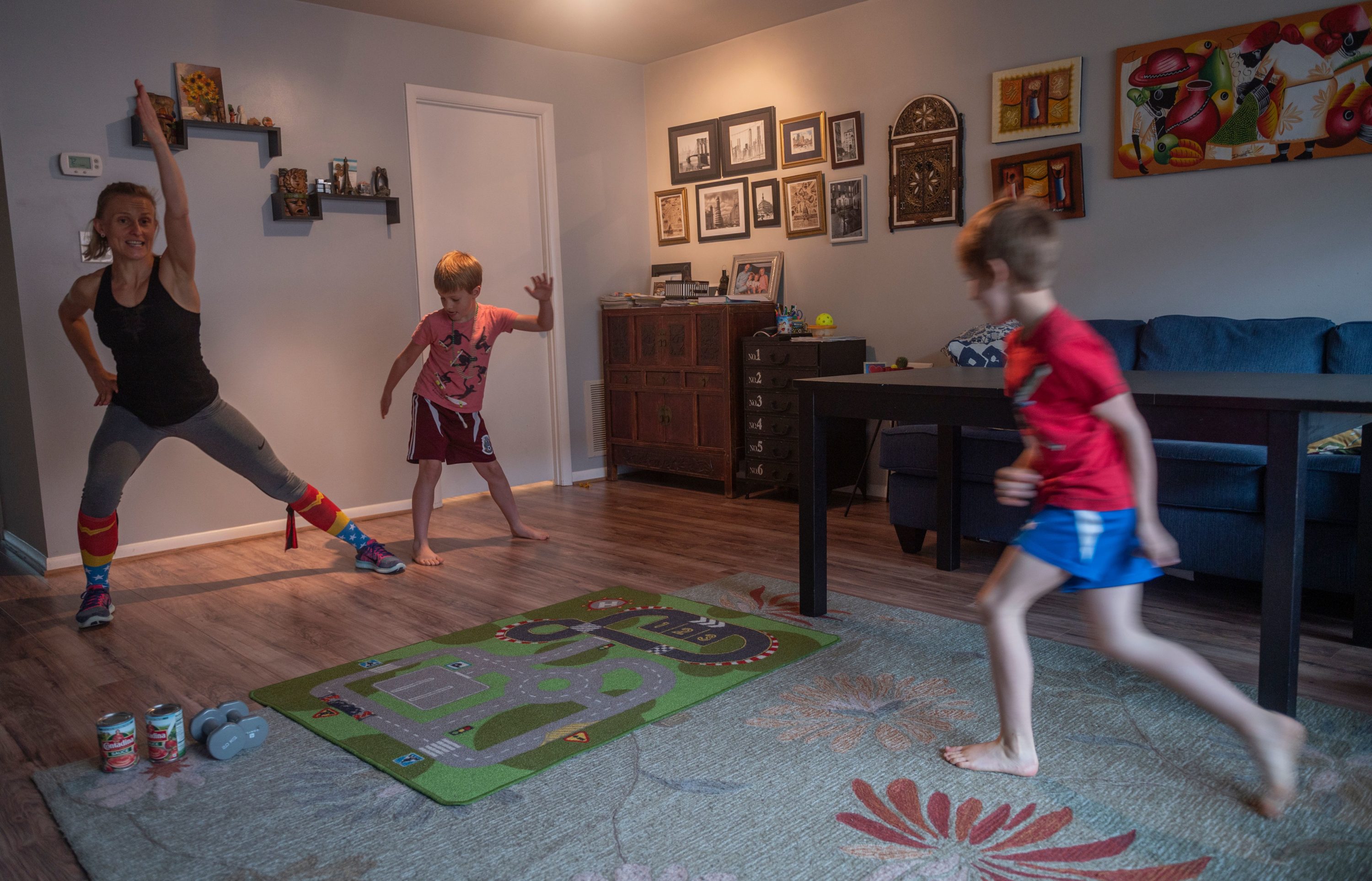 caption: Mimicked by her son Daniel (C), Paulina Mansz, a group fitness instructor, records a workout session for her clients while her other son Javier plays, as she continues to instruct from home in Arlington, Virginia on April 30, 2020. (Photo by ANDREW CABALLERO-REYNOLDS/AFP via Getty Images)