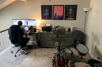 caption: Kevin Dole works from home next to his wife's bureau and near his drum set in the couple's small two-bedroom condo in Nashville, Tennessee.