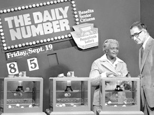 caption: Pennsylvania citizen Mary Ann Gilliam, left, is aided by Pennsylvania Lottery district manager Peter H. Cardiges as she picks a number for a lottery drawing on Sept. 19, 1980 in Pittsburgh.