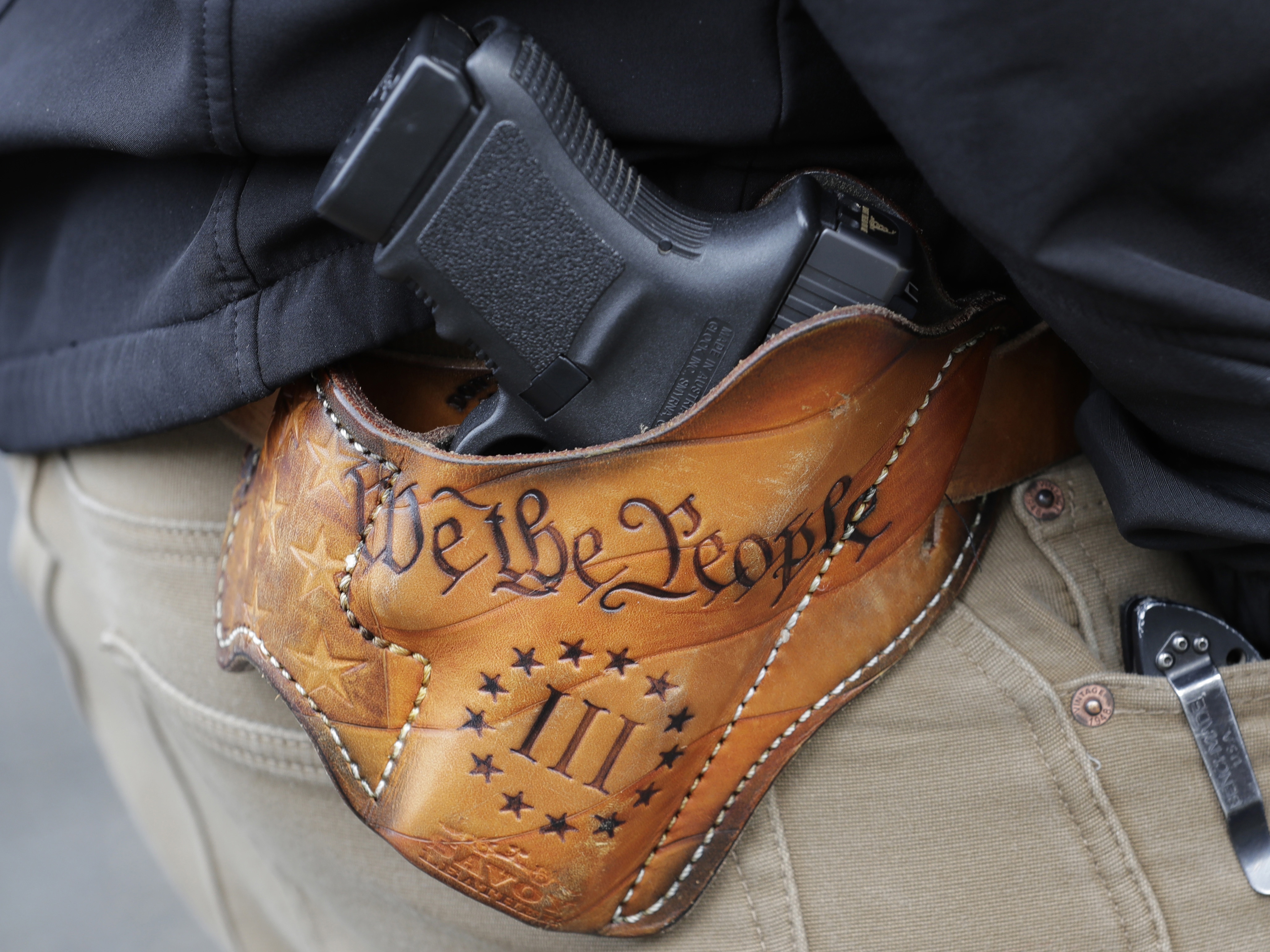 caption: An attendee at a gun rights rally open-carries his gun in a holster that reads "We the People," from the Preamble to the U.S. Constitution, in this 2019 photo at the Capitol in Olympia, Wash.