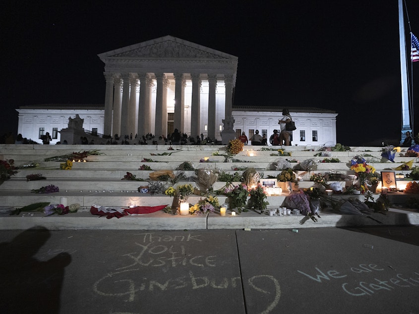 caption: The national flag flies at half staff as people gather to mourn the passing of Supreme Court Justice Ruth Bader Ginsburg at the steps in front of the Supreme Court.