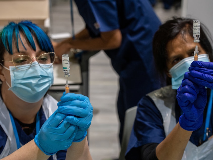 caption: Two health care workers prepare syringes with AstraZeneca's COVID-19 vaccine in London Monday. A U.K. study will expose volunteers to the coronavirus and could help development of future vaccines.
