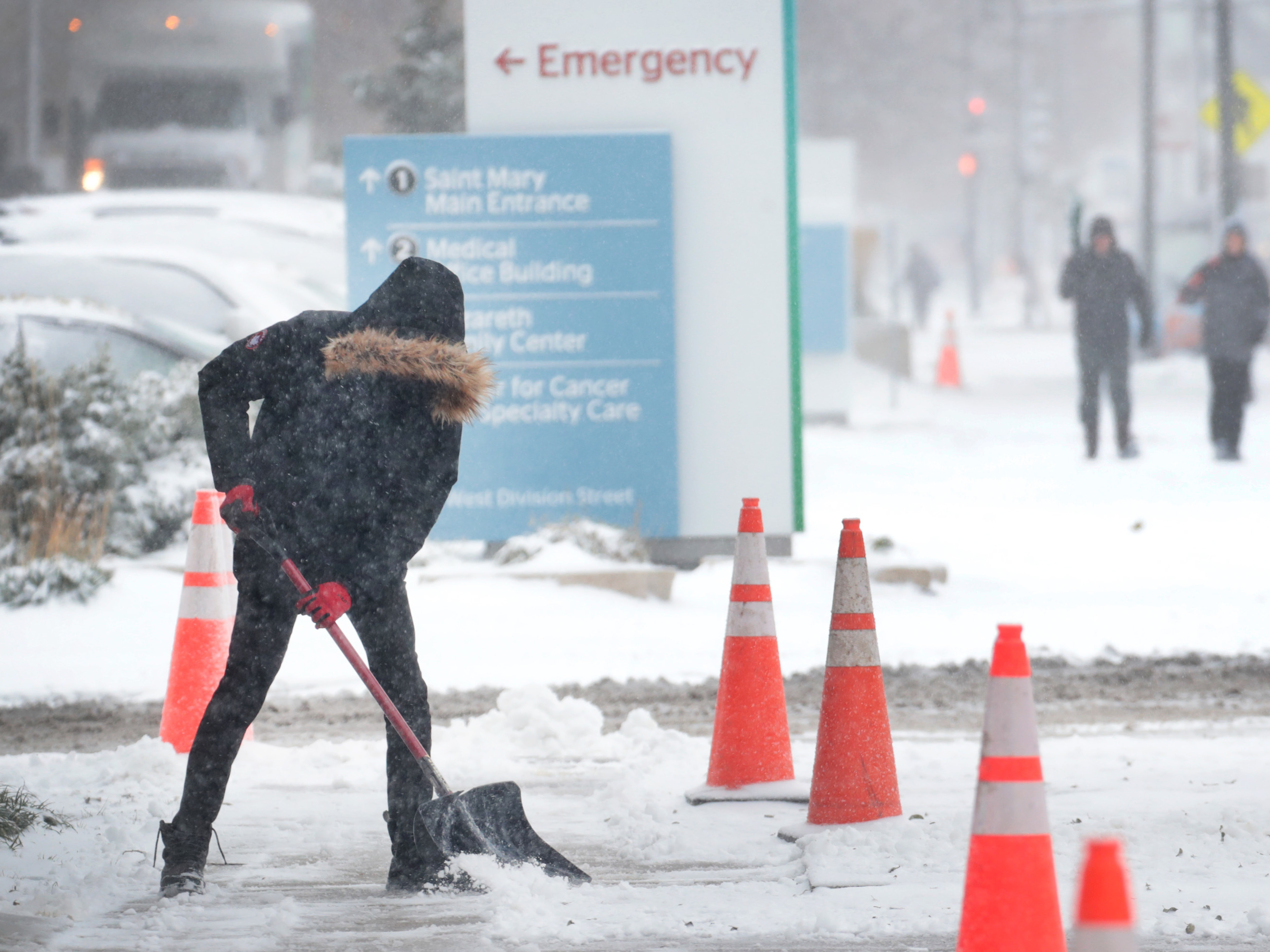 caption: A worker shovels snow from a sidewalk in the Humboldt Park neighborhood of Chicago. Forecasters expect temperatures to drop around 10 degrees by Wednesday.