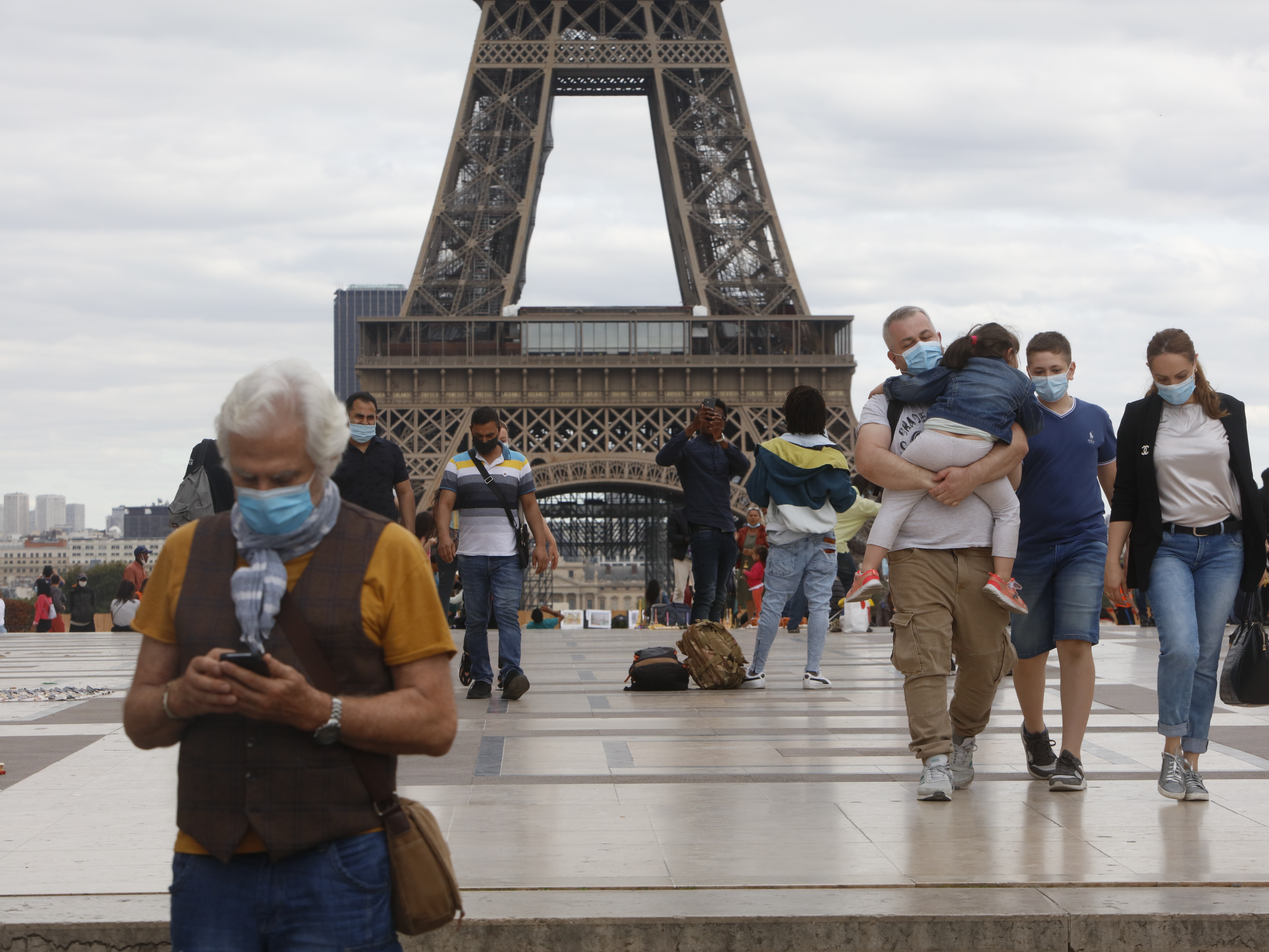 caption: People wearing masks walk near the Eiffel Tower in Paris on Thursday, the same day that the government made masks mandatory in all the city's public outdoor spaces.