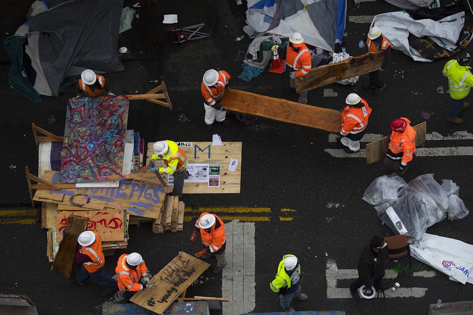 caption: Seattle Department of Transportation employees remove items from outside of the East Precinct building after the Capitol Hill Organized Protest zone was cleared by Seattle Police Department officers early Wednesday morning, July 1, 2020, in Seattle. 