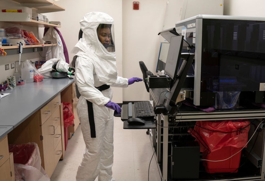 caption: Lab assistant Tammy Brown dons personal protective equipment in a lab at the University of Maryland School of Medicine in Baltimore. She works on preparing positive coronavirus tests for sequencing to discern variants rapidly spreading throughout the country.