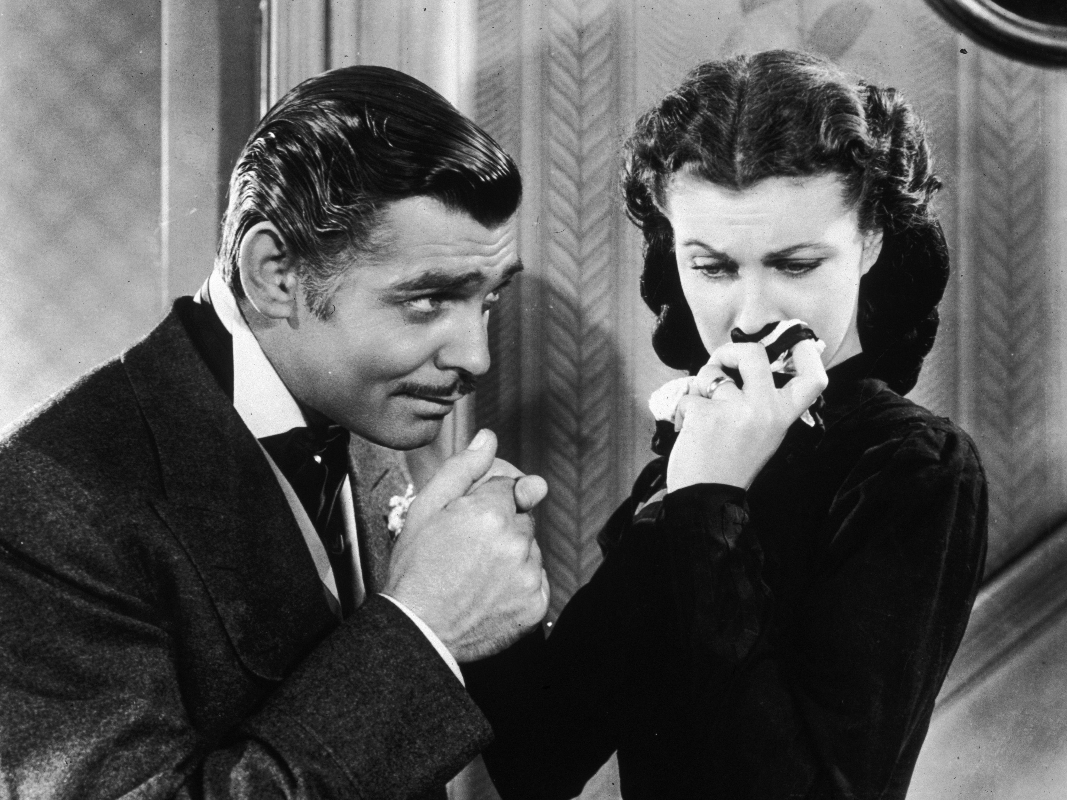 caption: American actor Clark Gable in his role as Rhett Butler kissing the hand of a tearful Scarlett O'Hara, played by Vivien Leigh in 'Gone With The Wind'.