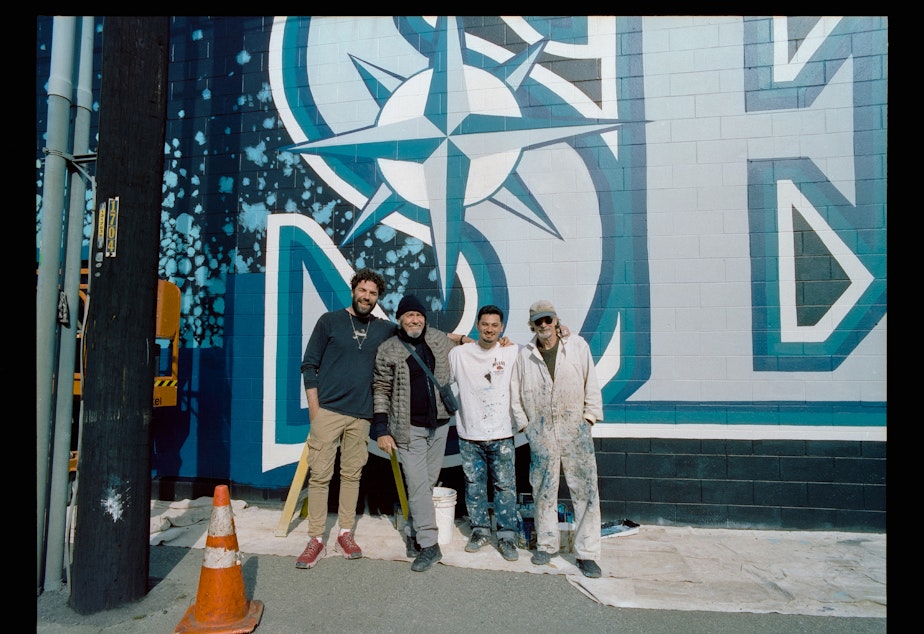 caption: From left: Nick Crespinel, James Crespinel, Alexander Codd, and Bob Codd standing in front of the mural they all worked on.