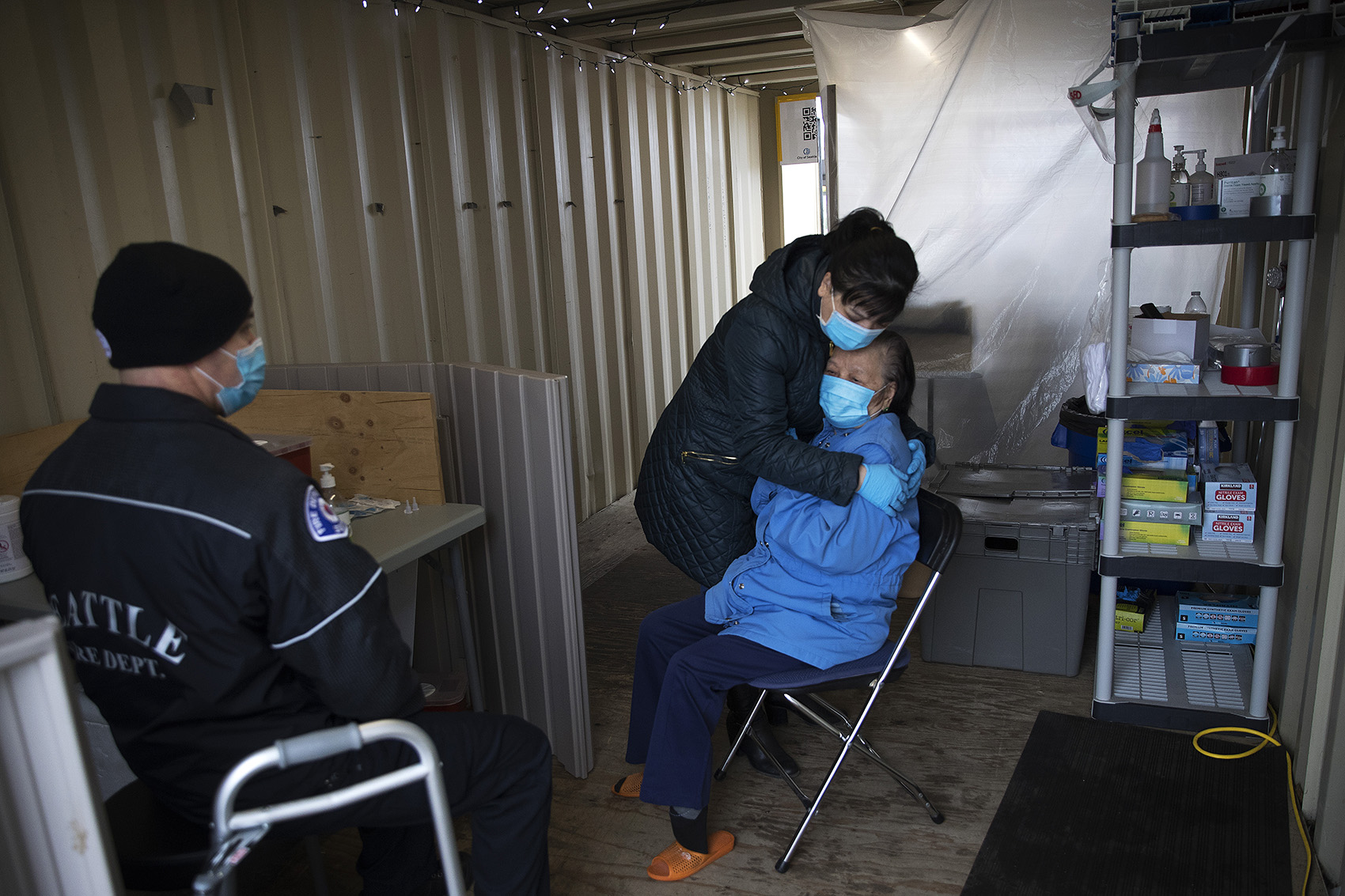 caption: Jennifer, who preferred to go by her first name only, hugs her mother, Du, 87, after she received her first dose of the Moderna Covid-19 vaccine, administered by Seattle Firefighter and EMT Dave Pedras, left, on Thursday, February 18, 2021, during a pop-up vaccination clinic at the West Seattle Covid-19 testing site on Southwest Thistle Street in Seattle.