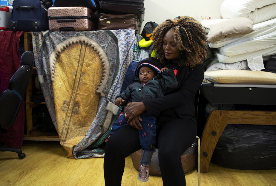caption: Madidi Mbala of Angola holds her 10-month-old daughter in a common area of the Riverton Park United Methodist Church, where nearly 200 people are sheltering while seeking asylum, on Monday, Oct. 16, 2023, in Tukwila. 