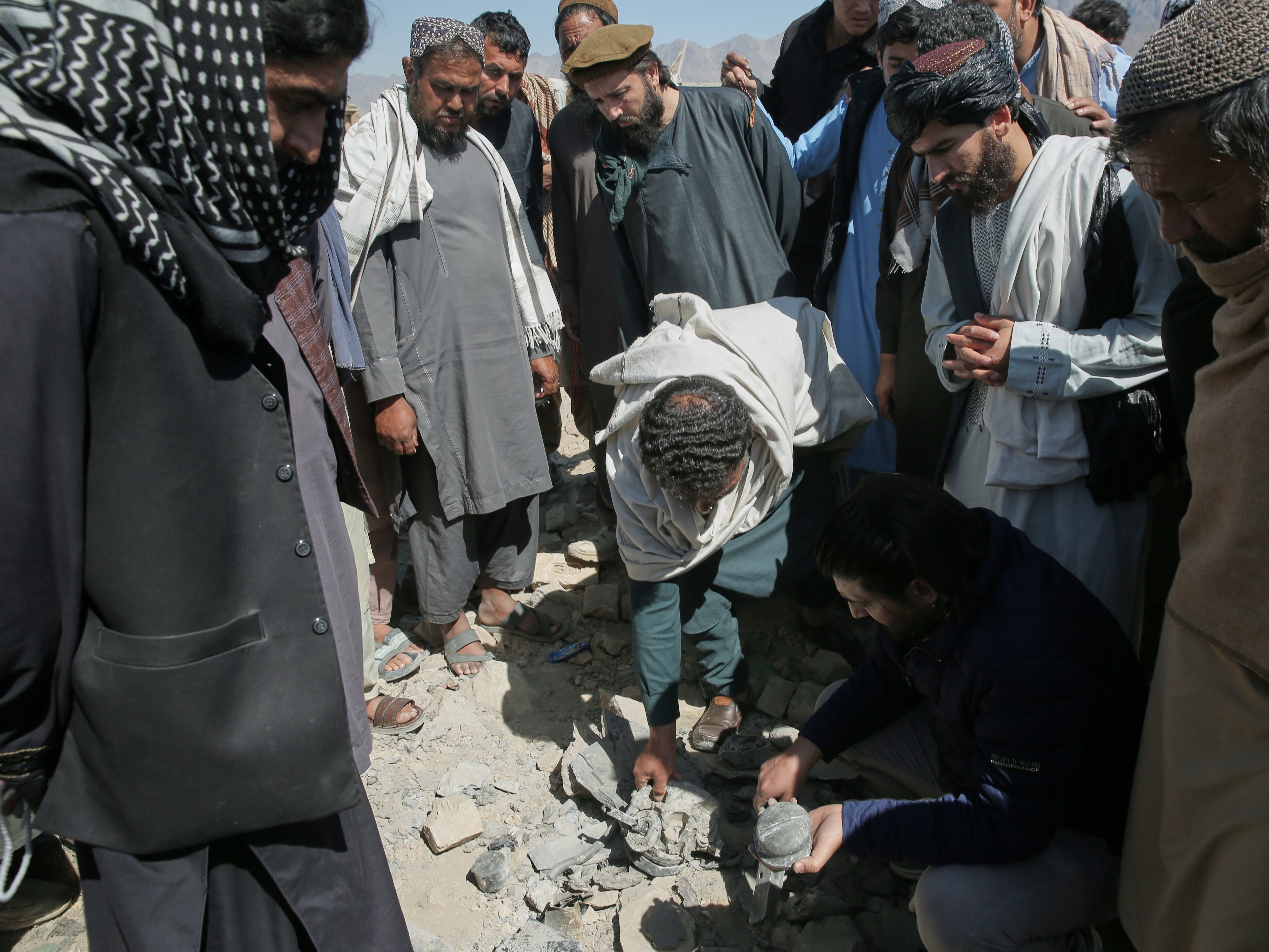 caption: Residents and Taliban police gather the remains of a projectile at the site of a strike in Kabul, Afghanistan, on March 13.
