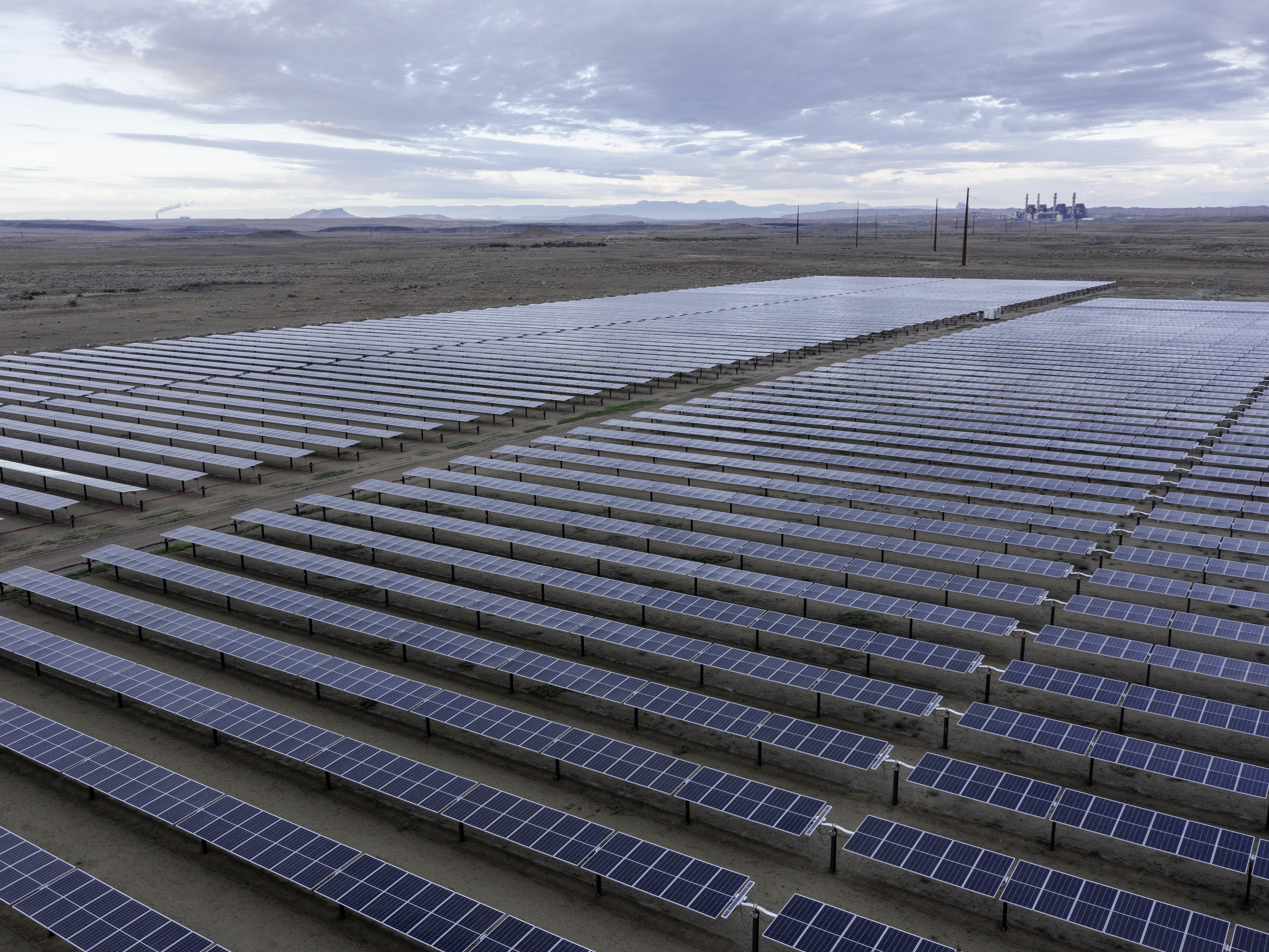 caption: Panels that are part of San Juan Solar Project in northern New Mexico, with San Juan Generating Station smokestacks in the distance