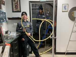 caption: Danny Luckman and Aidan Czerniak of Simply Installs Heating & Air Conditioning cut out and remove natural gas lines from a tattoo and piercing shop. To meet climate change goals, Ithaca, New York wants to switch from gas to electric in the city's 6000 buildings.