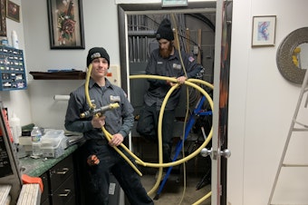 caption: Danny Luckman and Aidan Czerniak of Simply Installs Heating & Air Conditioning cut out and remove natural gas lines from a tattoo and piercing shop. To meet climate change goals, Ithaca, New York wants to switch from gas to electric in the city's 6000 buildings.