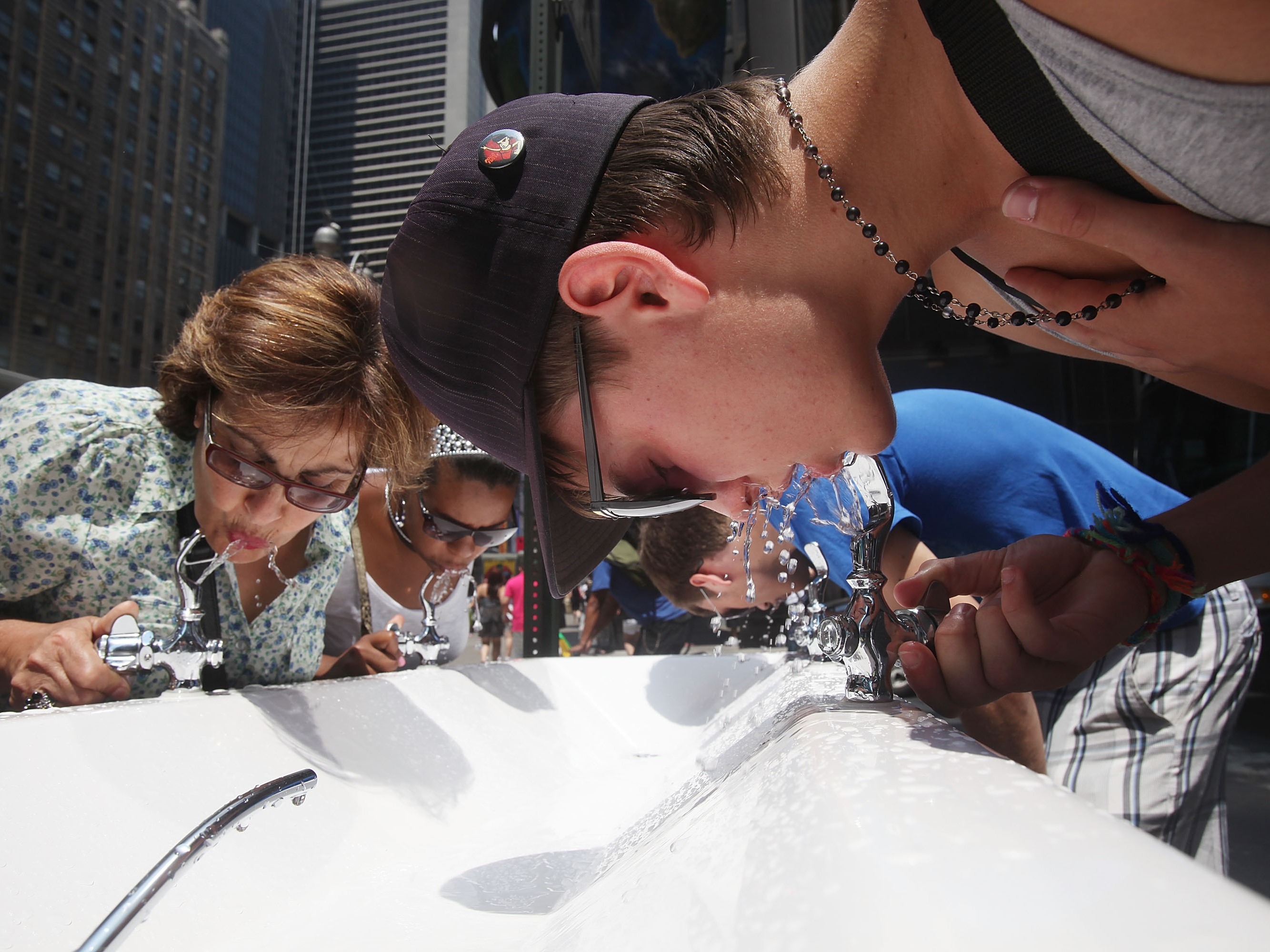 caption: People drink water from a water fountain in New York City on July 7, 2010.