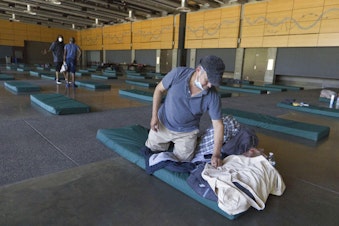 caption: Roberto Cedomio prepares his bed at a cooling shelter run by the Salvation Army at the Seattle Center during a heat wave hitting the Pacific Northwest, Sunday, June 27, 2021, in Seattle. Seattle set a record high for the day. Cedomio said he was glad to have this place available in the heat. 