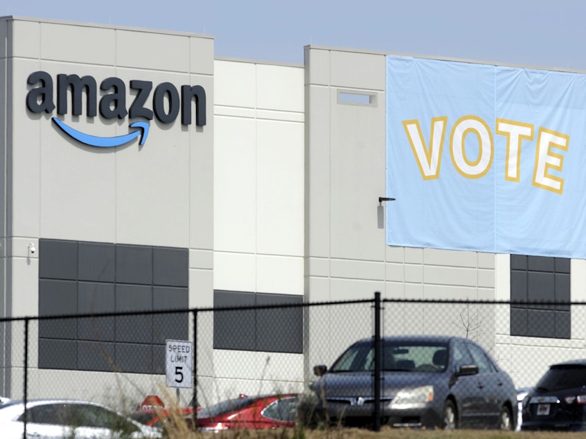 caption: A banner encouraging workers to vote in labor balloting is shown at an Amazon warehouse in Bessemer, Ala., on March 30. The company has reached a settlement with the National Labor Relations Board to allow its workers to organize freely and without retaliation.
