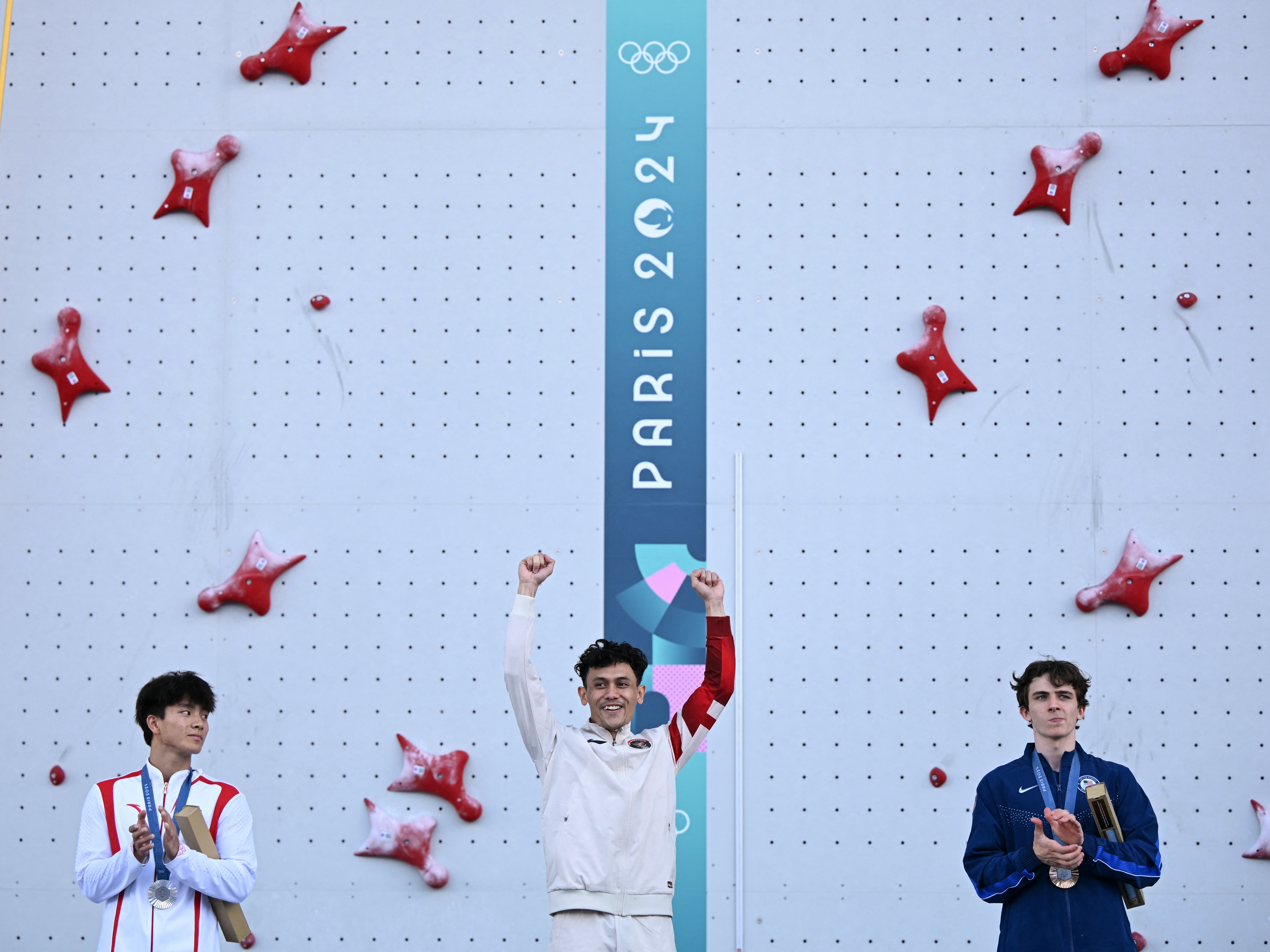 caption: Gold medalist Indonesia's Veddriq Leonardo (center), silver medallst China's Wu Peng (left) and bronze medalist UsA's Sam Watson (right) pose on the podium of the men's sport climbing speed event during the Paris Olympics at the Le Bourget Sport Climbing Venue northeast of Paris.