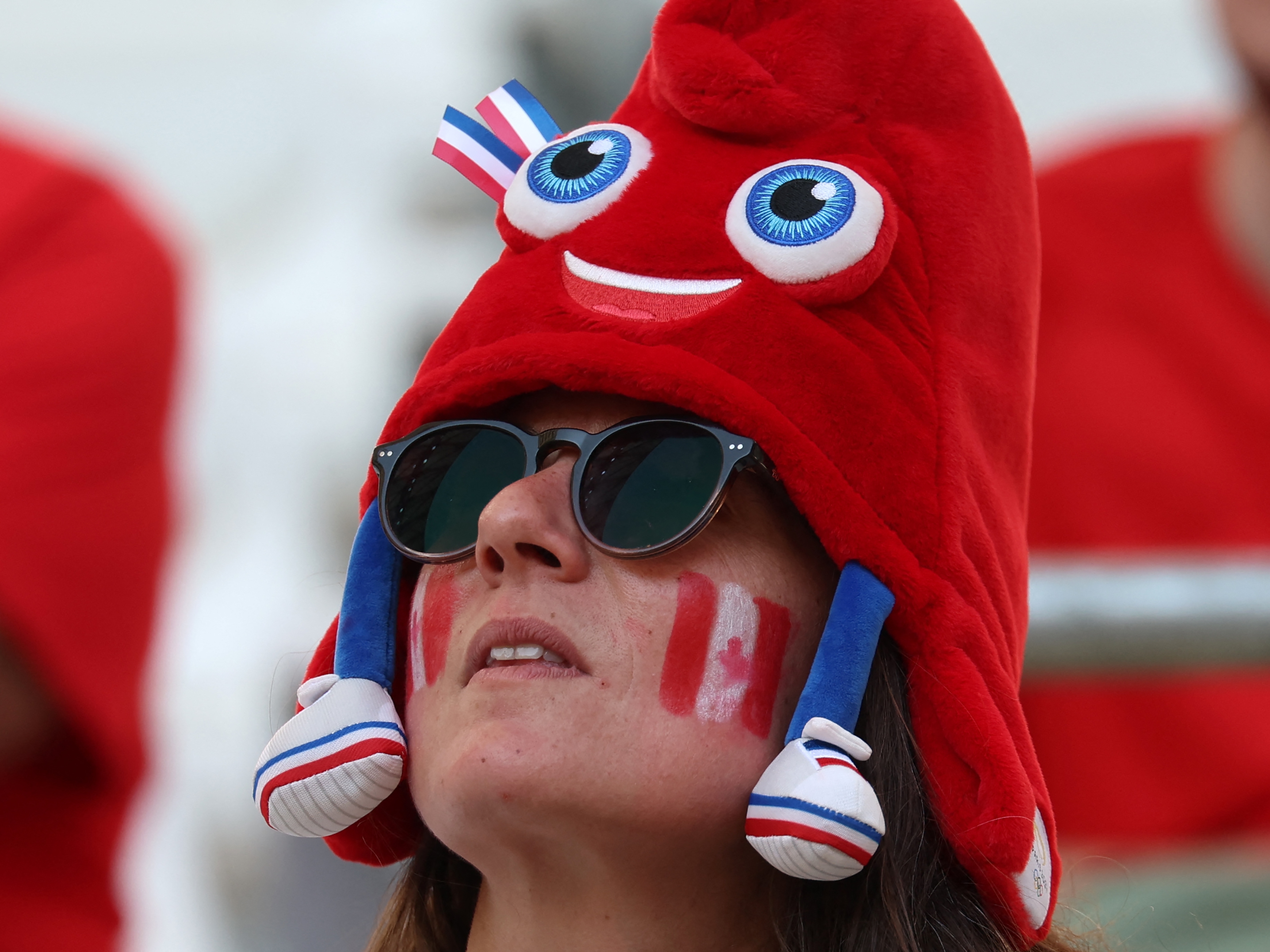 caption: A Canada fan dons an Olympic mascot Phryge hat before the women's quarter-final football match between Canada and Germany during the Paris Olympics.