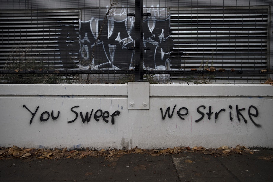 caption: 'You sweep we strike' is painted near the perimeter of an encampment where unhoused community members reside on Wednesday, December 16, 2020, ahead of a scheduled sweep by the Seattle Police Department at Cal Anderson Park in Seattle.