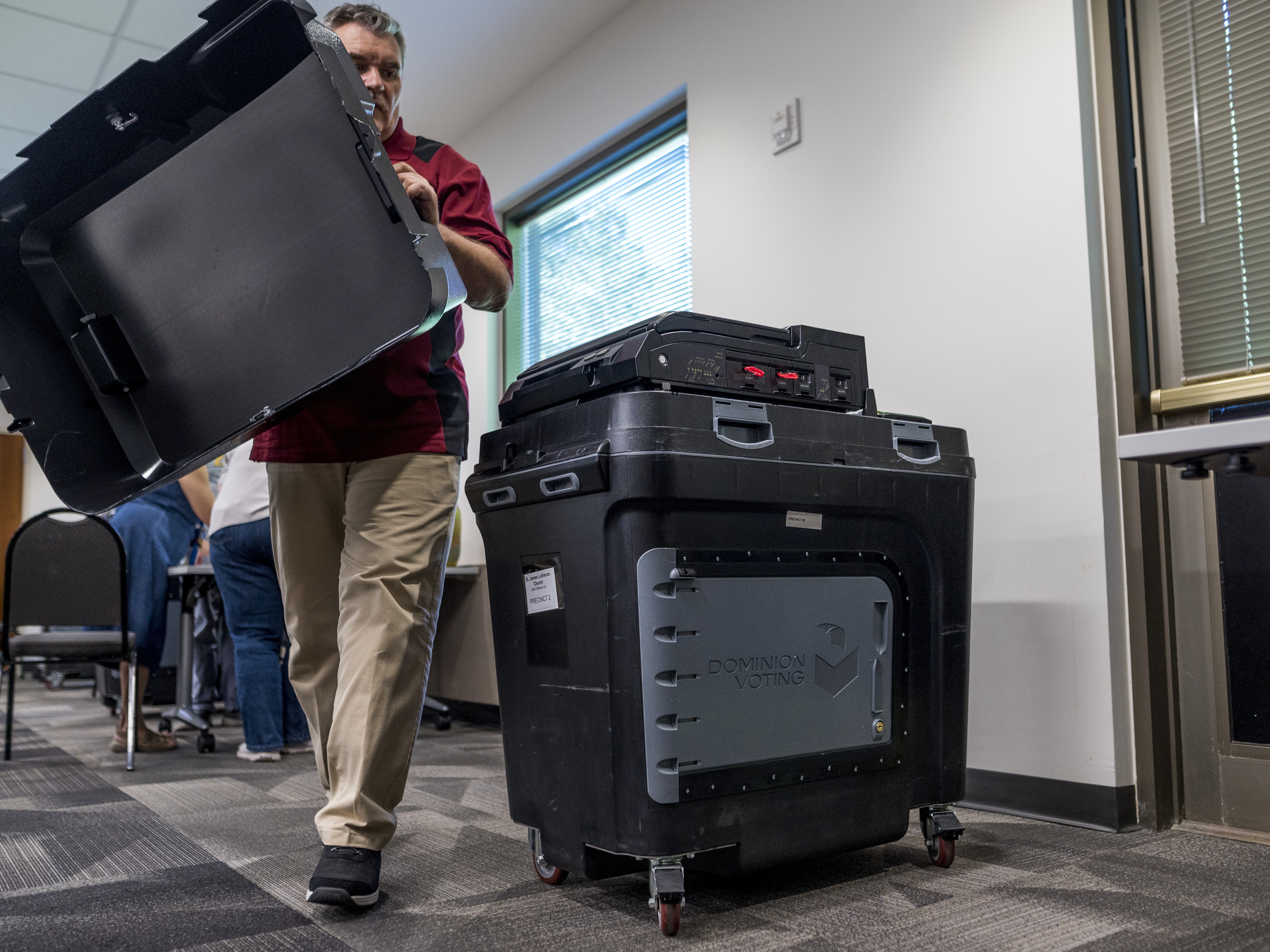 caption: An election judge sets up a Dominion voting machine during a public accuracy test of voting equipment on Aug. 3, 2022, in Burnsville, Minn.