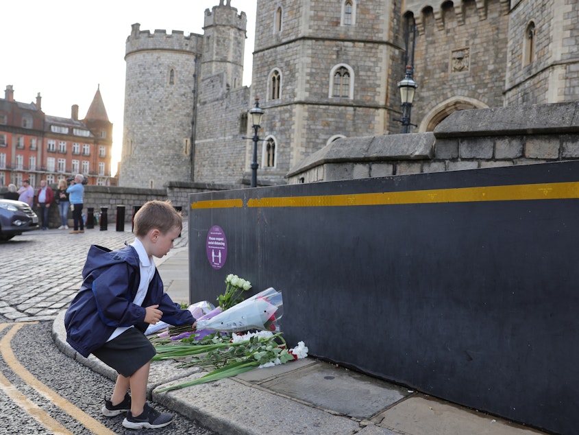 caption: Queen Elizabeth II's death sets a succession apparatus in motion that has been dormant for decades. Here, a youngster leaves flowers outside Windsor Castle on Thursday.