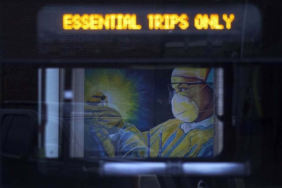 caption: A mural of a health care worker is shown through the window of a passing King County Metro bus on Tuesday, April 28, 2020, along South Main Street in Seattle.