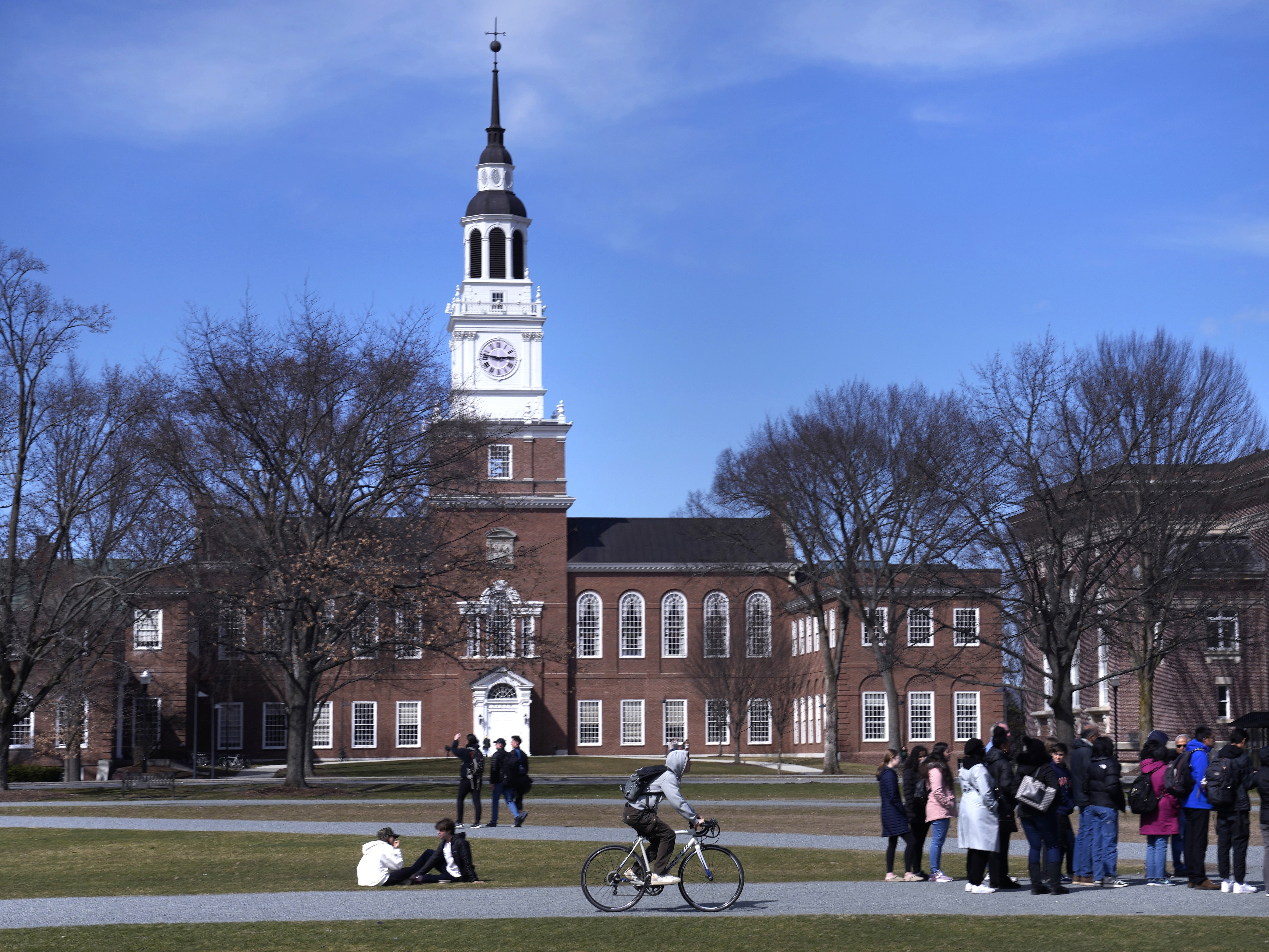caption: A bicyclist passes a college tour group outside the Baker Library at Dartmouth College, April 7, 2023, in Hanover, N.H.