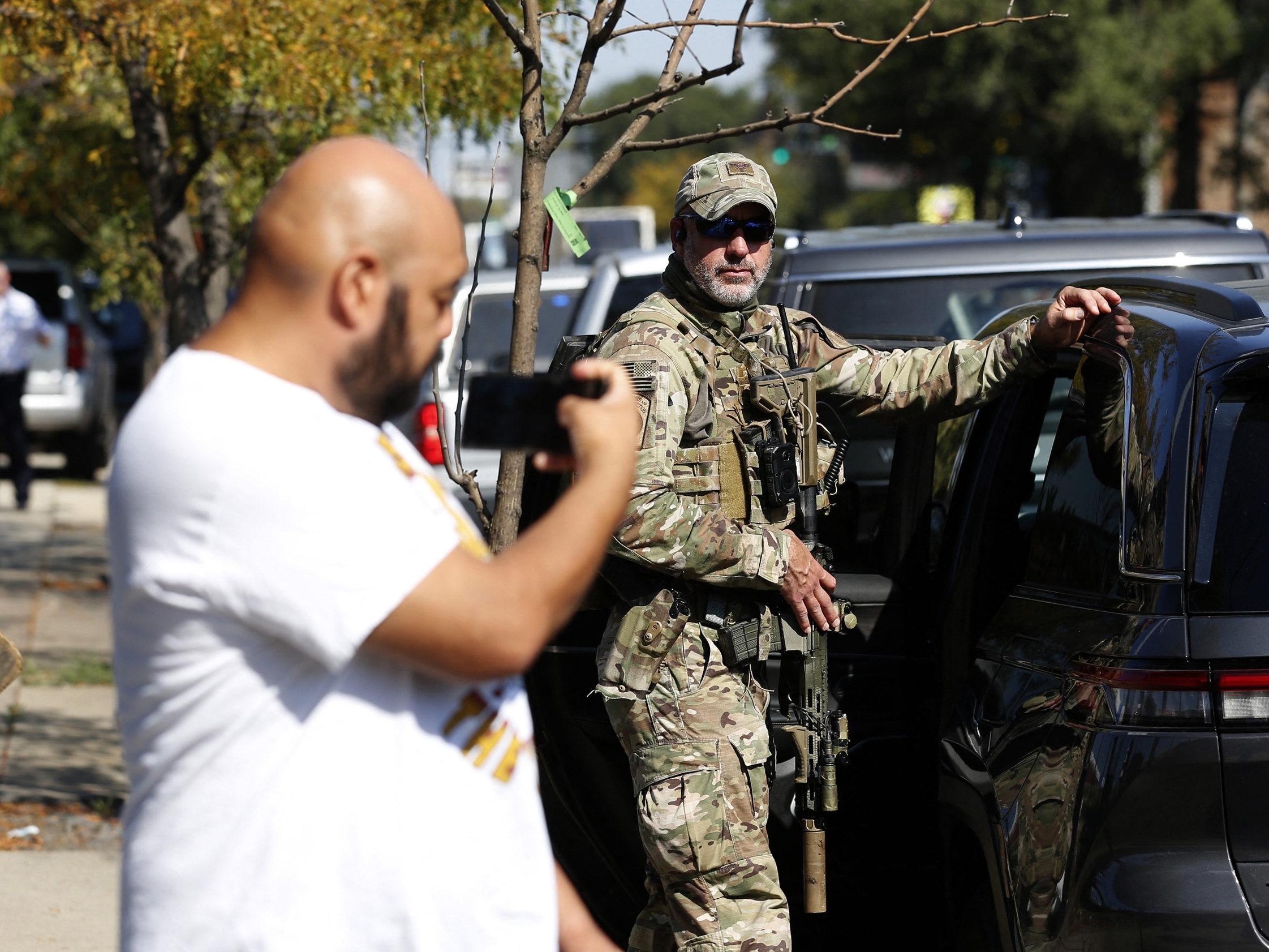 caption: A man holds his phone up next to a U.S. Customs and Border Protection (CBP) Border Patrol agent during an immigration raid in Chicago on Oct. 4, 2025. The top official of CBP's sister agency, Immigration and Customs Enforcement, confirmed last week that the agency is using powerful spyware that can hack into phones.