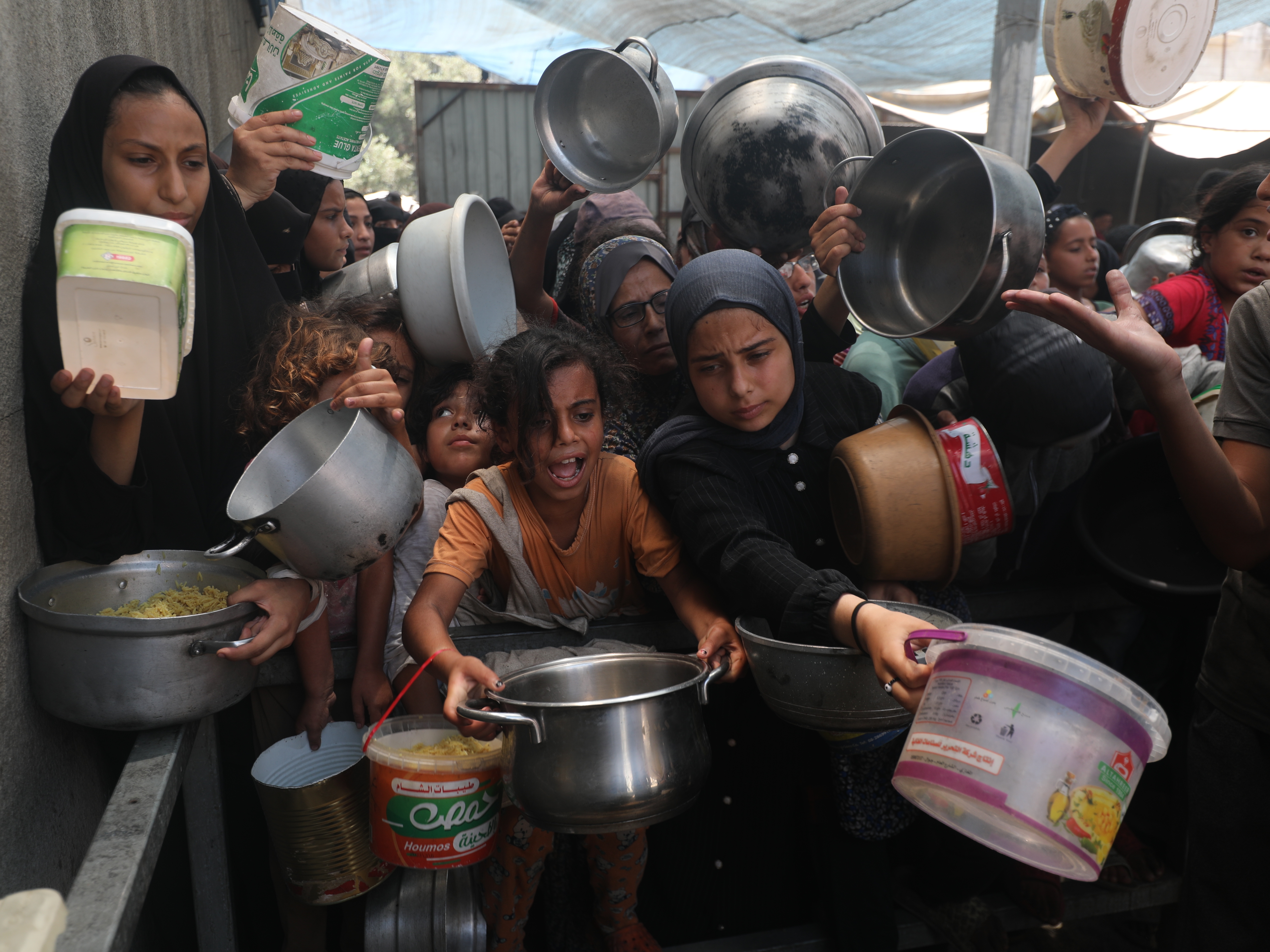 caption: Palestinians, including children, who are struggling to access food due to Israel's blockade and ongoing attacks on the Gaza Strip, wait in line to receive food.