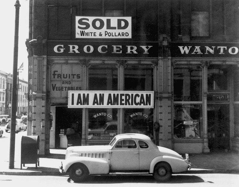 caption: A large sign reading "I am an American" is displayed in the window of a Japanese-owned grocery store, the day after the attack onPearl Harbor.