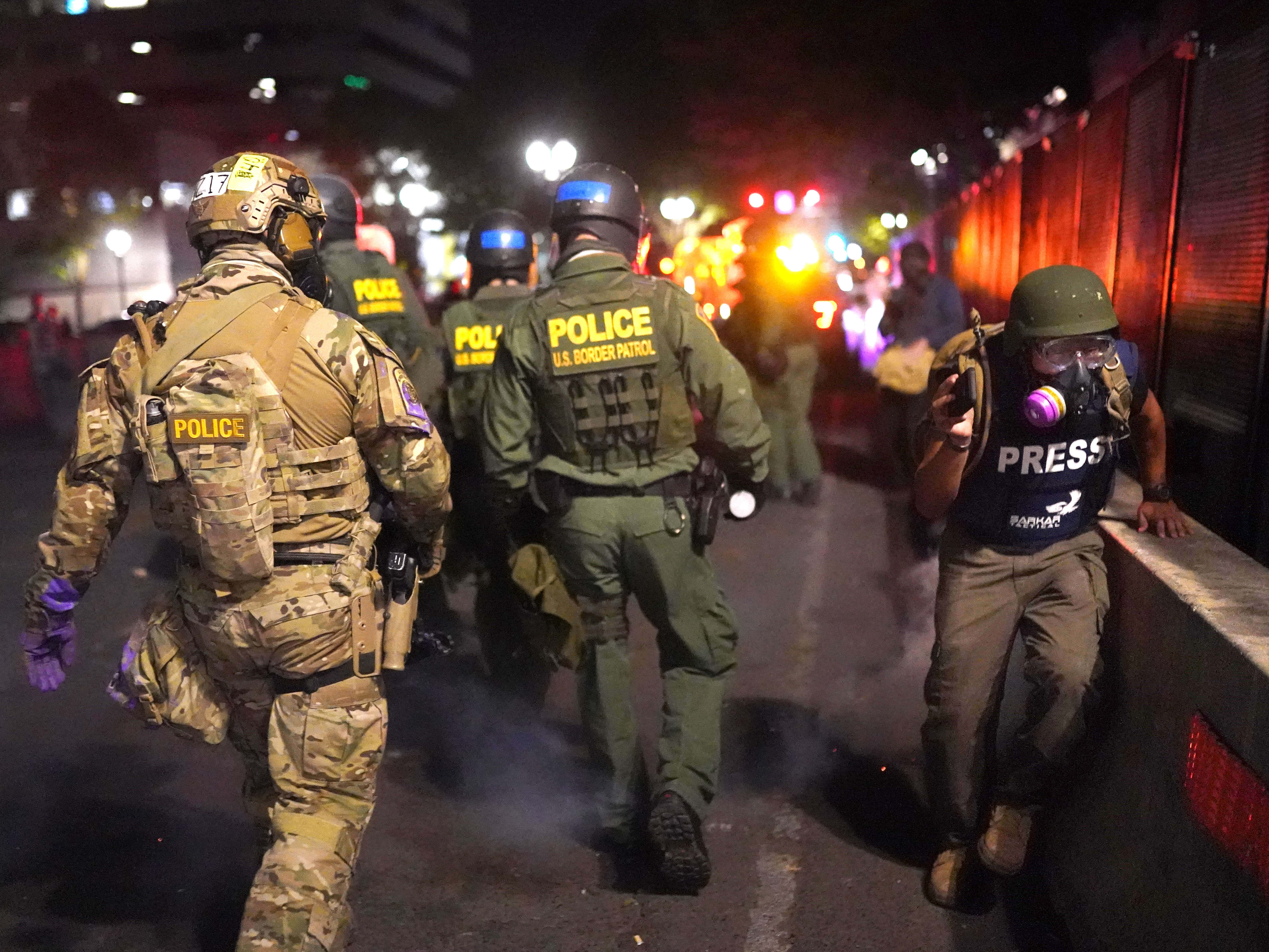 caption: A journalist runs past federal officers during a protest against racial injustice in front of the Mark O. Hatfield U.S. Courthouse on July 30 in Portland, Ore.