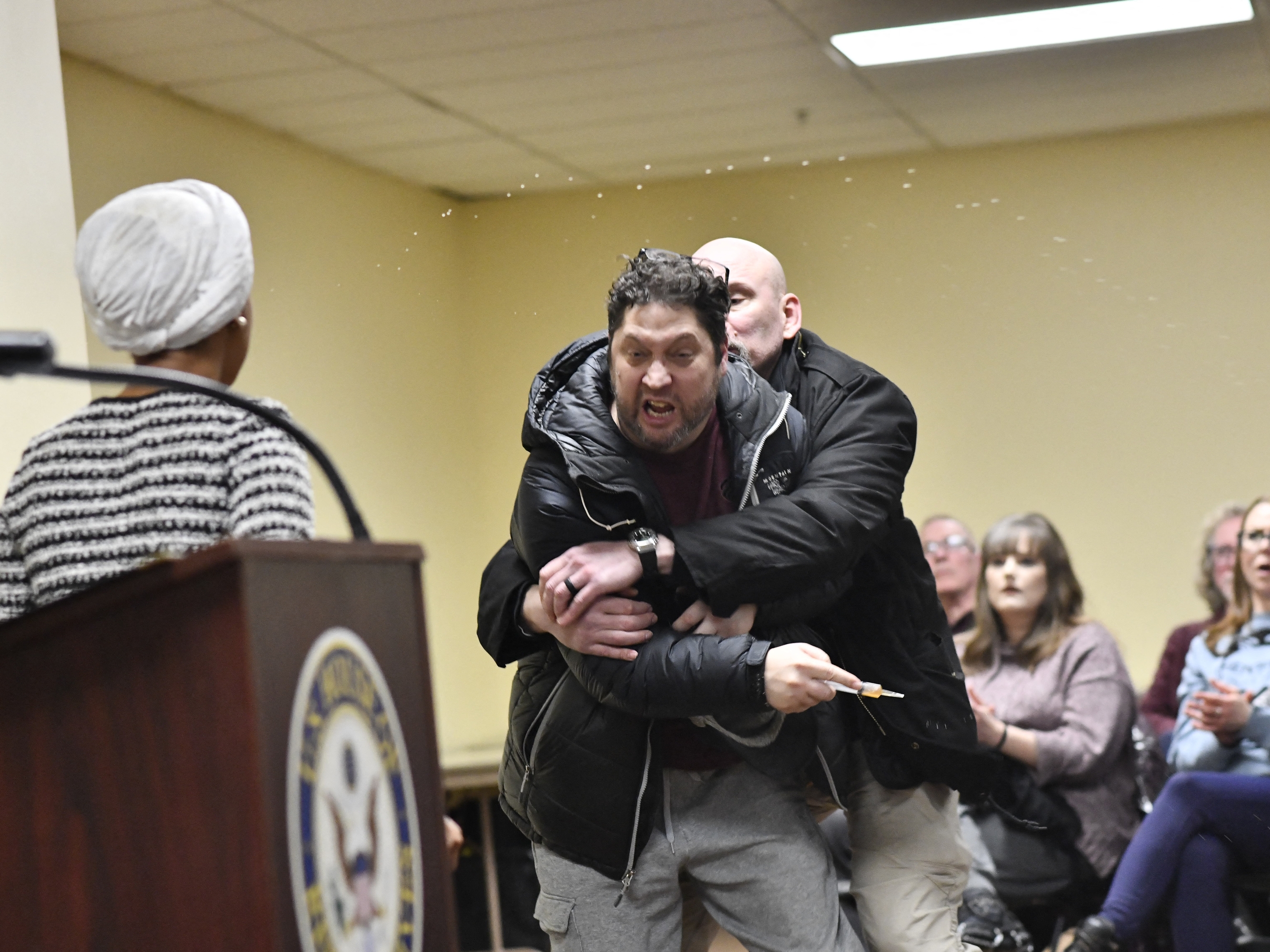 caption: A man is tackled after spraying an unknown substance at US Representative Ilhan Omar (D-MN) (L) during a town hall she was hosting in Minneapolis, Minnesota, on January 27, 2026. (Photo by Octavio JONES / AFP via Getty Images)