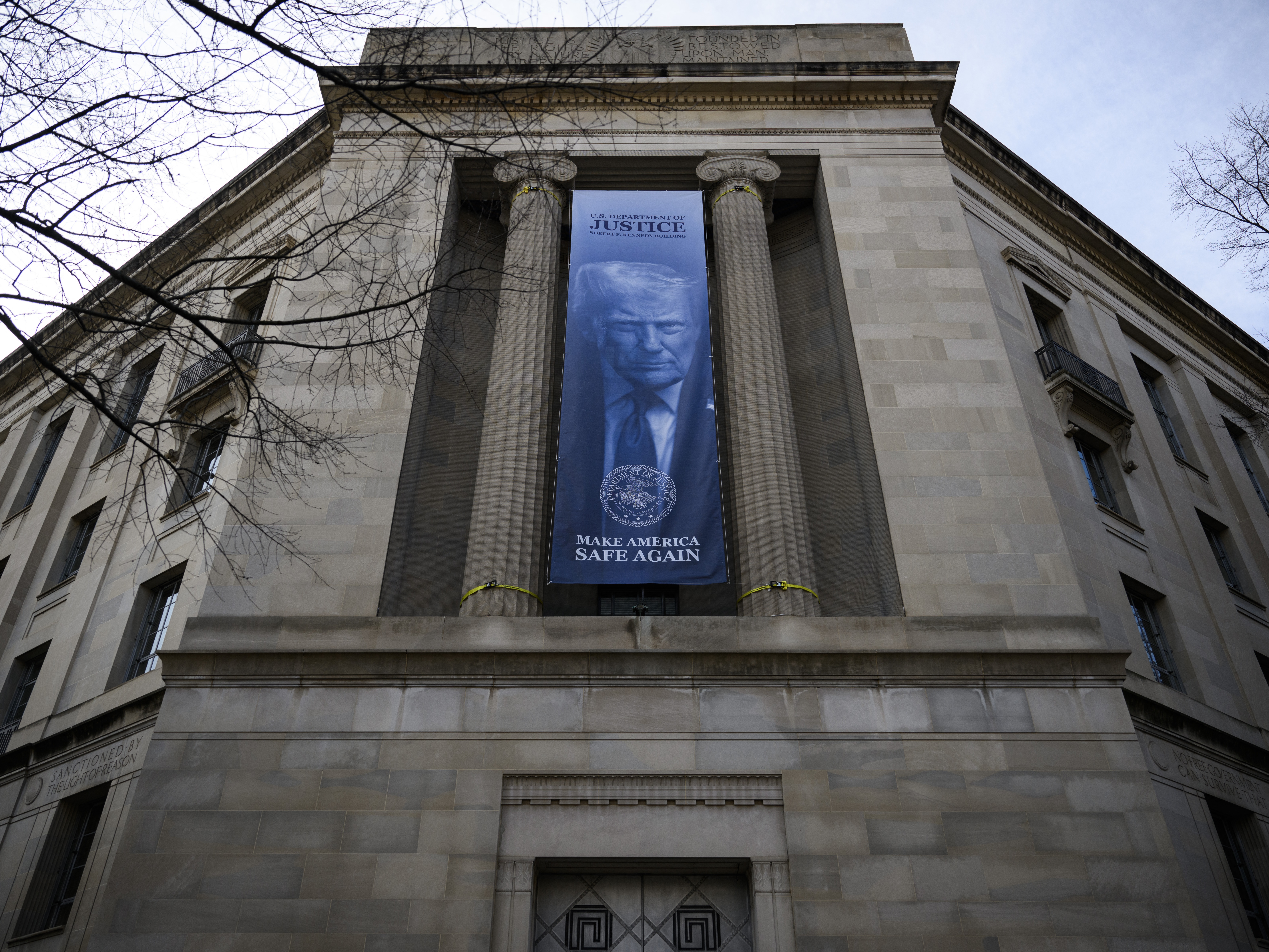 caption: A banner featuring an image of President Trump is displayed on the facade of the Department of Justice headquarters in Washington, D.C. The Justice Department has been trying to force states to hand over sensitive voter data that it plans to share with the Department of Homeland Security.