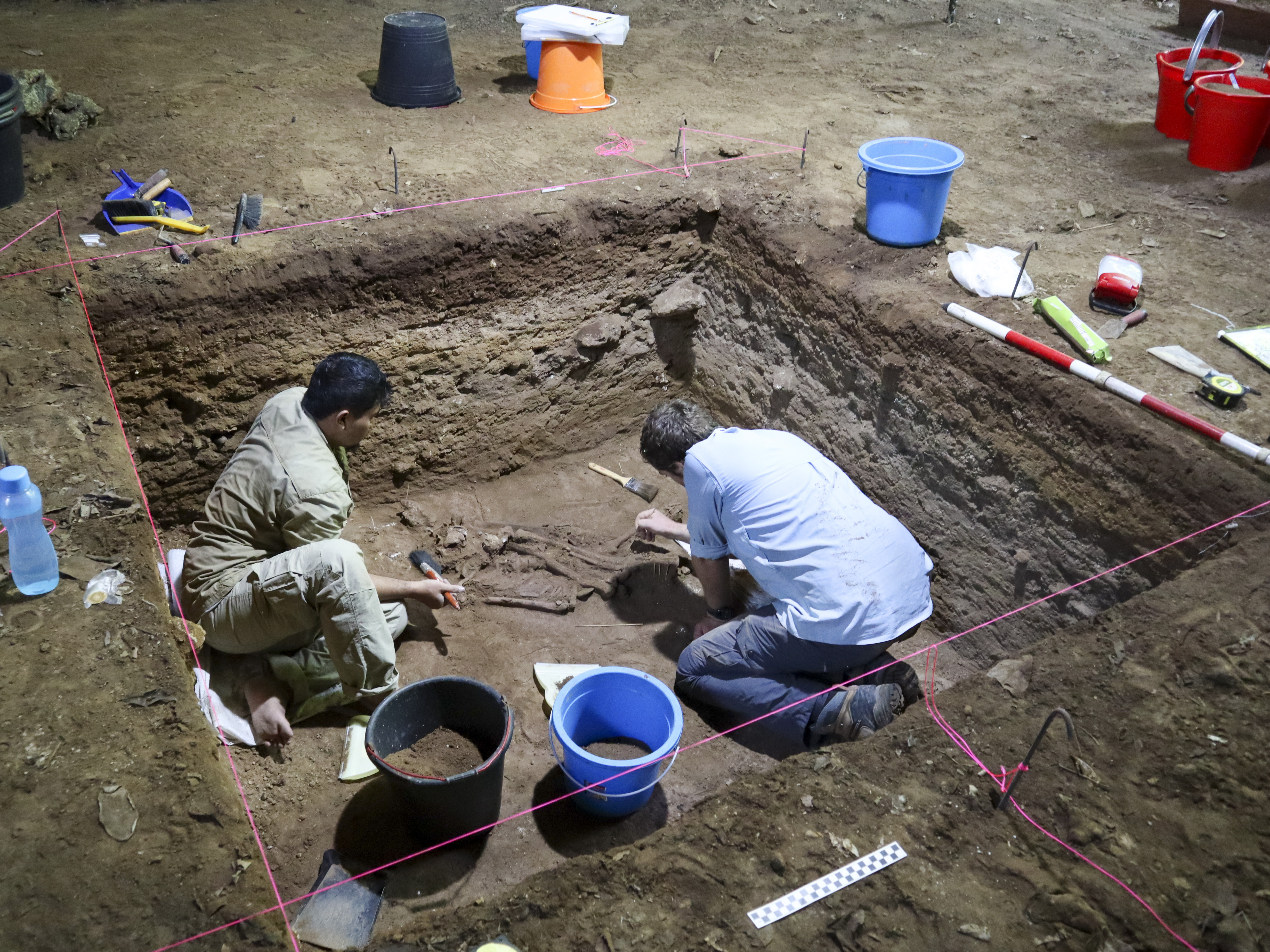 caption: Dr. Tim Maloney and Andika Priyatno work at the site in a cave in East Kalimantan, Borneo, Indonesia, on March 2, 2020. The remains, which have been dated to 31,000 years old, mark the oldest evidence for amputation yet discovered.