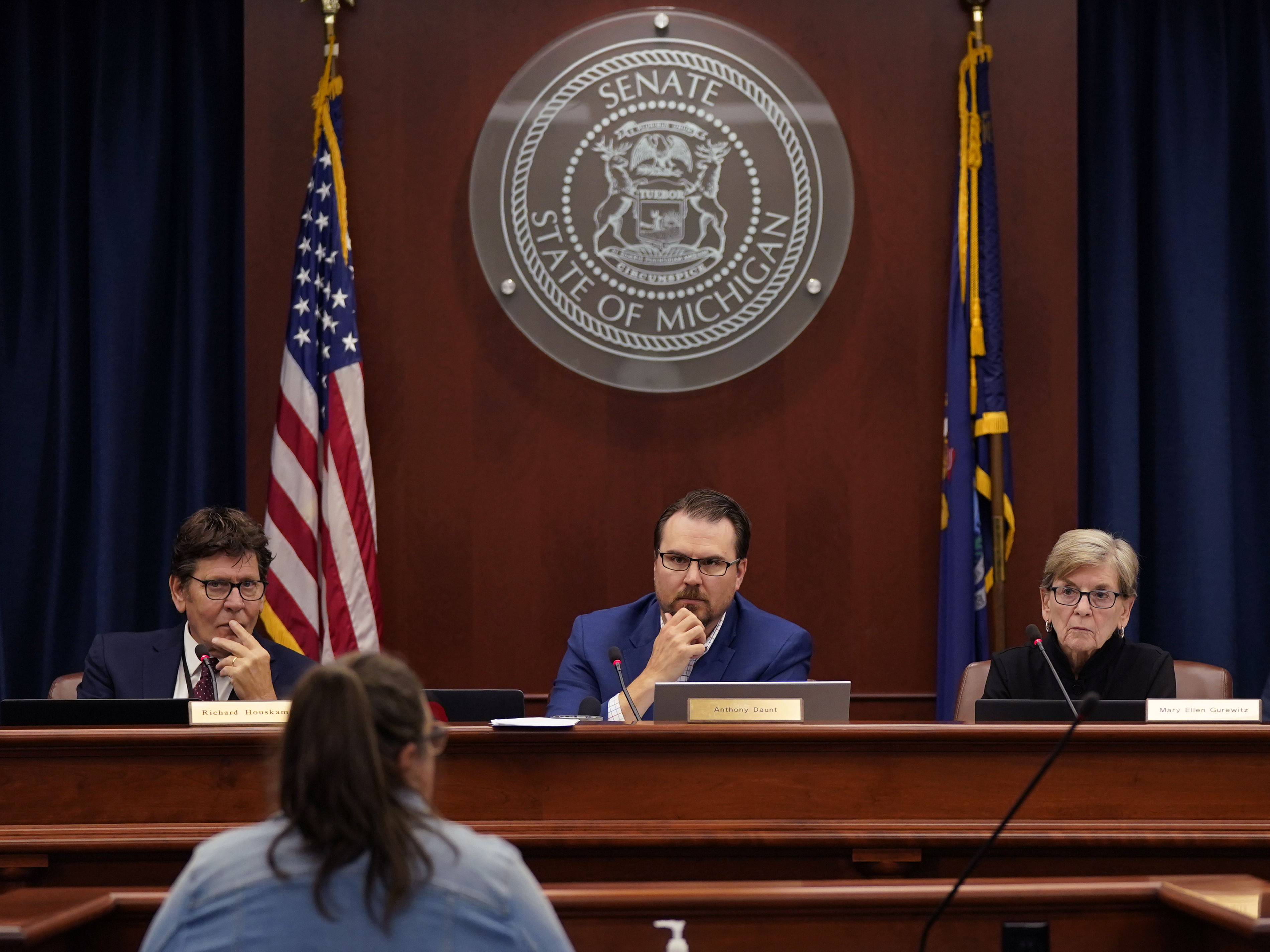 caption: Richard Houskamp, left, Anthony Daunt and Mary Ellen Gurewitz, members of the Michigan state Board of Canvassers, listen to a speaker during a hearing.