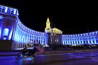 caption: An American flag unfurls off a pedicab as it glides past the Denver City/County Building, which is illuminated in yellow and blue in support of Ukraine on Monday. Colorado's State Capitol will also be illuminated in blue and yellow in support of Ukraine.