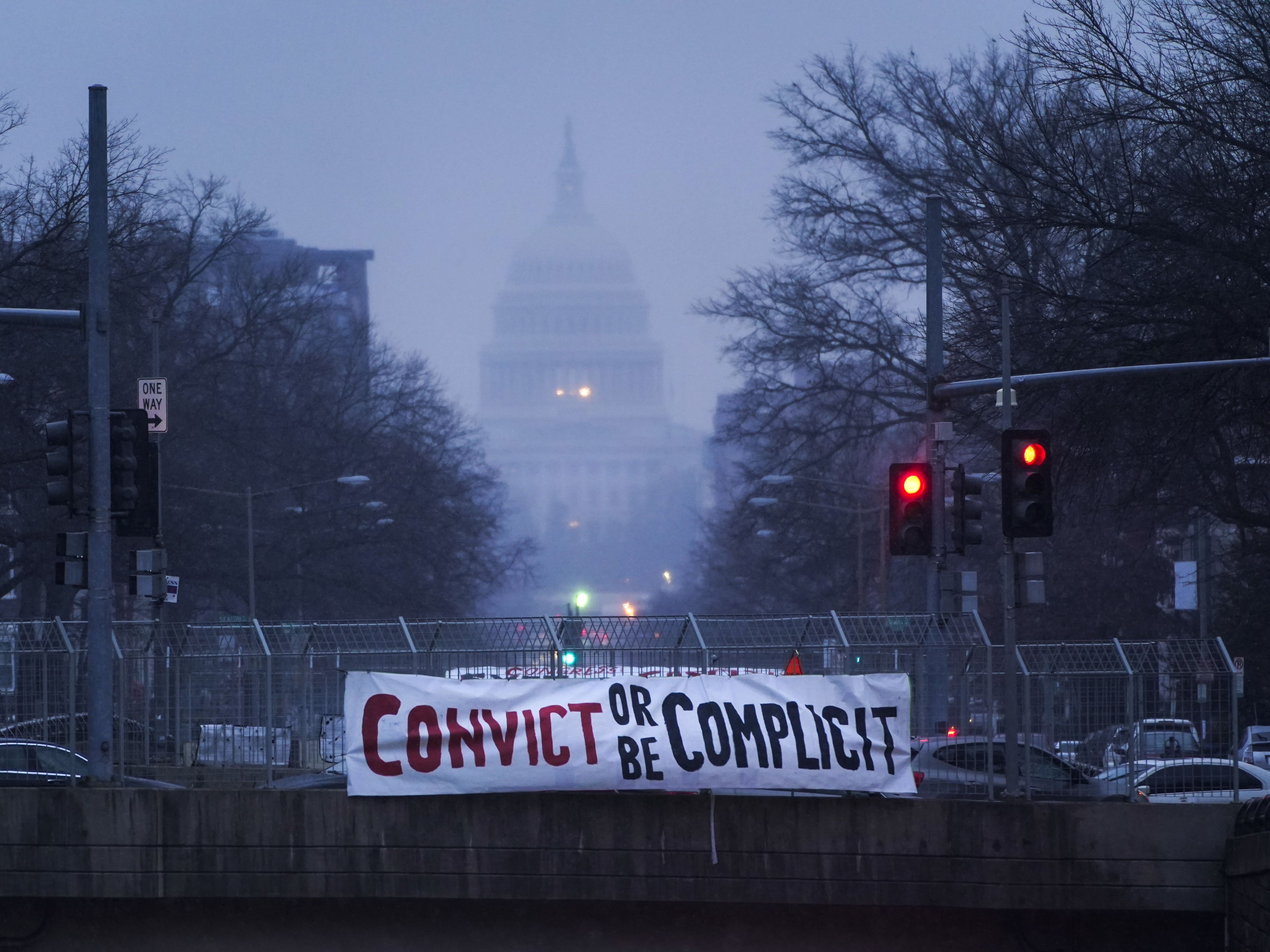 caption: A sign reading "Convict or Be Complicit" hangs from a bridge on North Capitol Street in Washington, D.C., on the second day of former President Donald Trump's second impeachment trial.