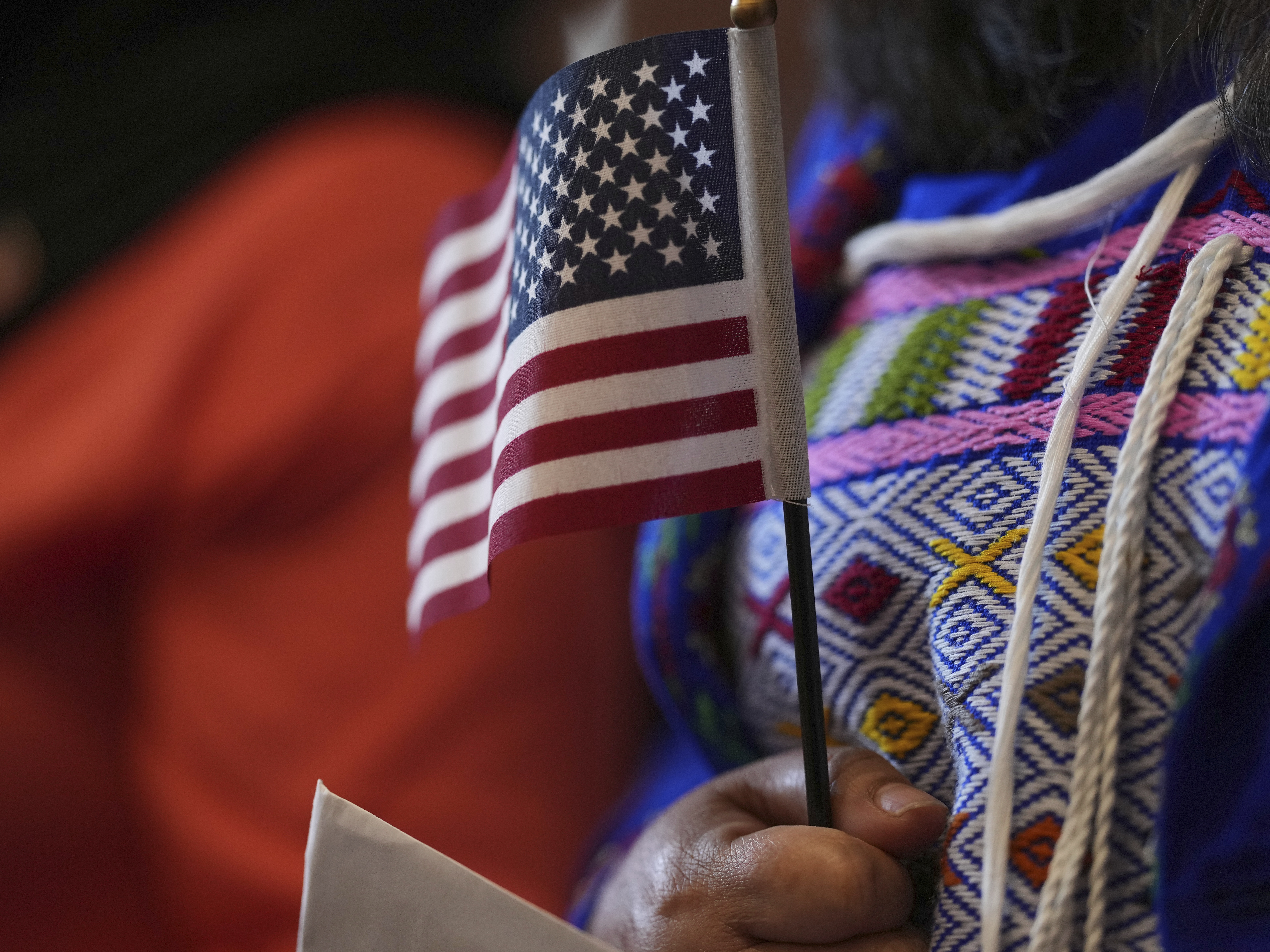 caption: A woman clutches a U.S. flag as she and applicants from 20 countries prepare to take an oath of citizenship in commemoration of Independence Day during a naturalization ceremony in San Antonio in July 2025.