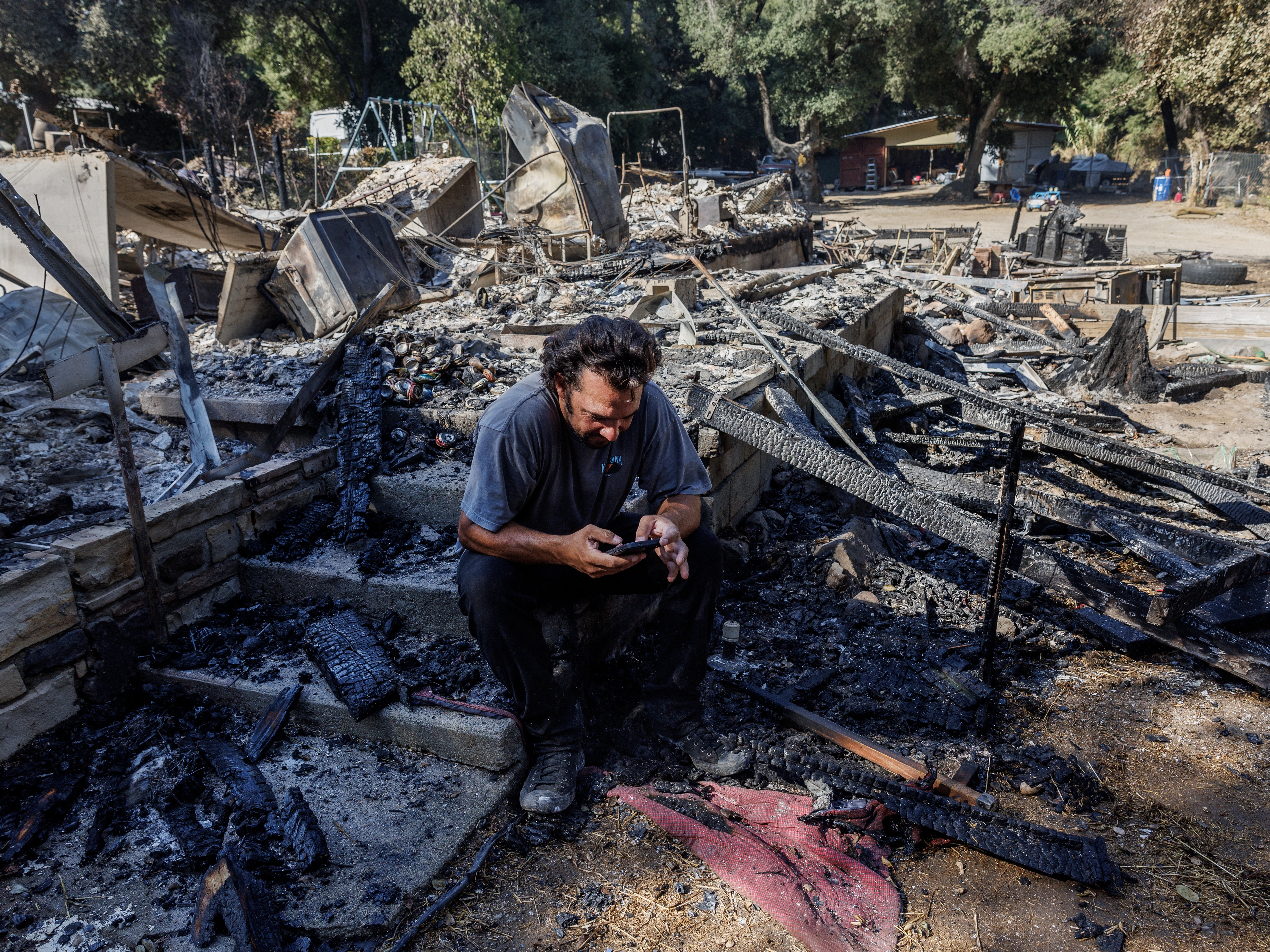 caption: Garrett Keene sits on the front steps of his home in Lake Elsinore, Calif. that was destroyed in the Airport Fire, one of three major Southern California Fires so far this September. After evacuating with his family, Keene said he monitored the Watch Duty fire app to see where airdrops of fire retardant were happening as the fire approached, but none dropped on his neighborhood.