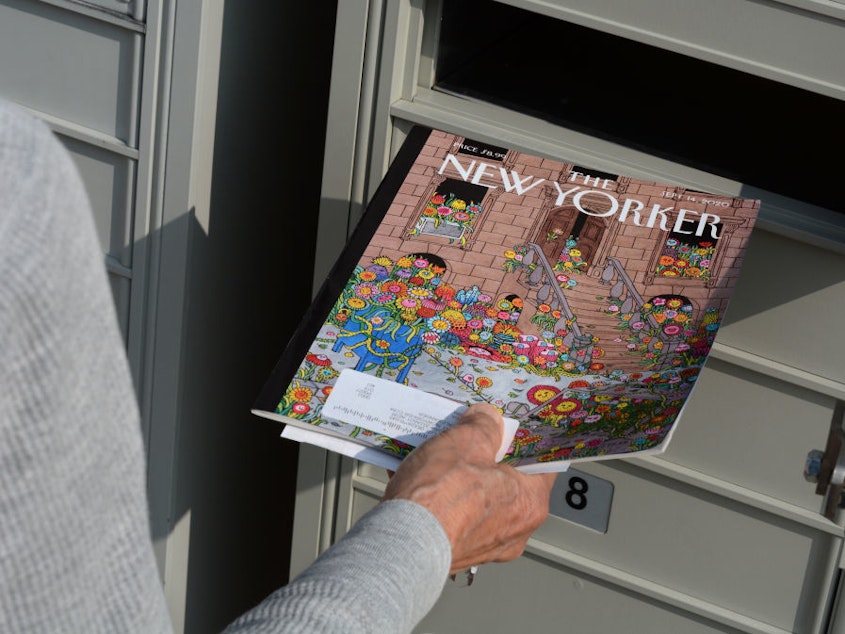 caption: A woman retrieves a copy of <em>The New Yorker</em> magazine from her mailbox in Santa Fe, N.M. in 2020.