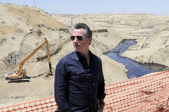 caption: Gov. Gavin Newsom tours the Chevron oil field west of Bakersfield, where a spill of more than 800,000 gallons flowed into a dry creek bed in McKittrick, Calif. in July 2019.