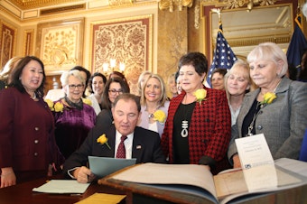 caption: Utah Gov. Gary Herbert signs bill honoring the state's pioneering women suffragists on Wednesday. He's surrounded by state senators and representatives, and his wife, who are all wearing the yellow rose symbolizing suffrage.<em> </em>