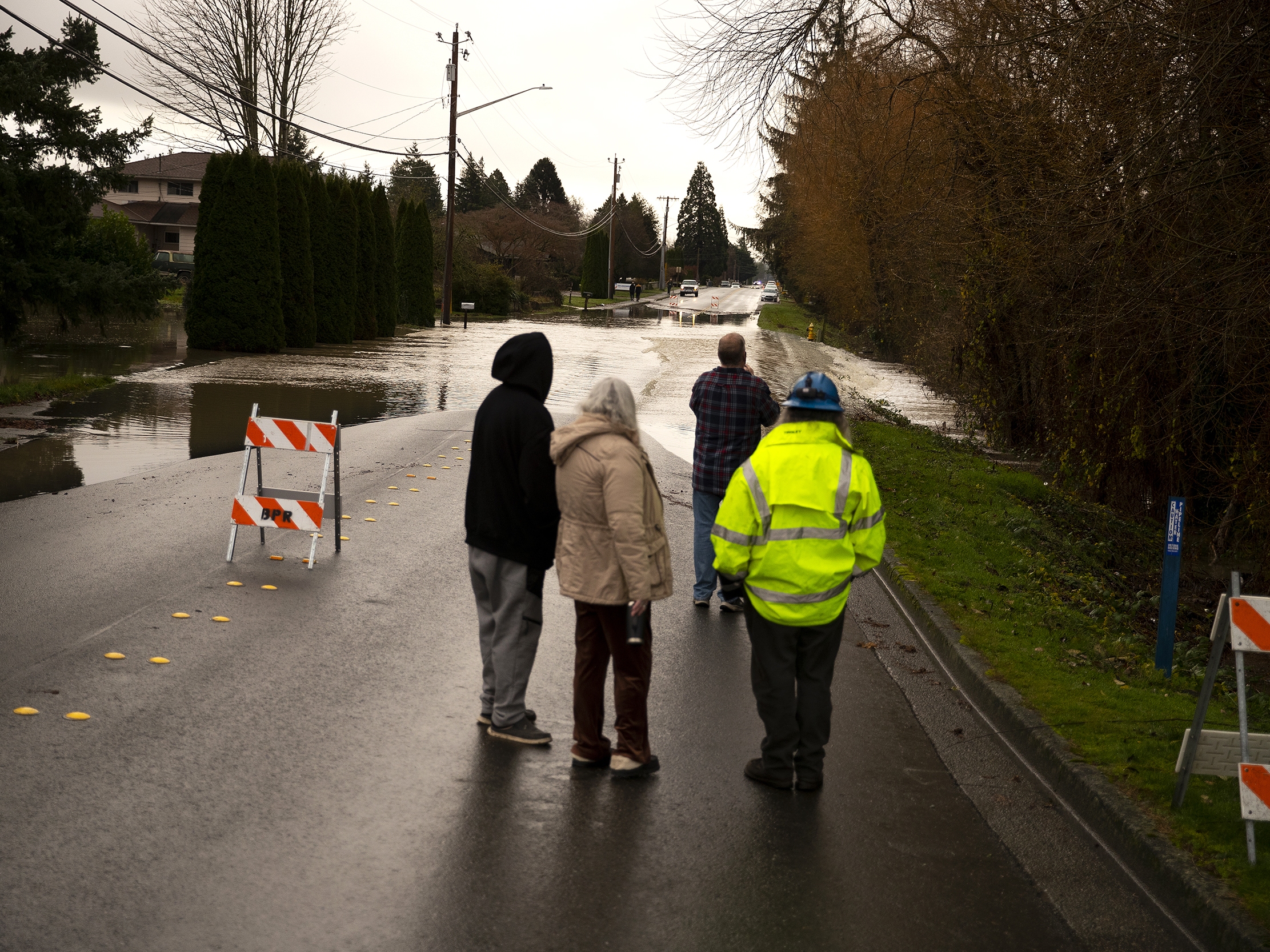 caption: Neighbors watch as Gages Slough overflows and floods a street in Burlington, Wash., on Friday.