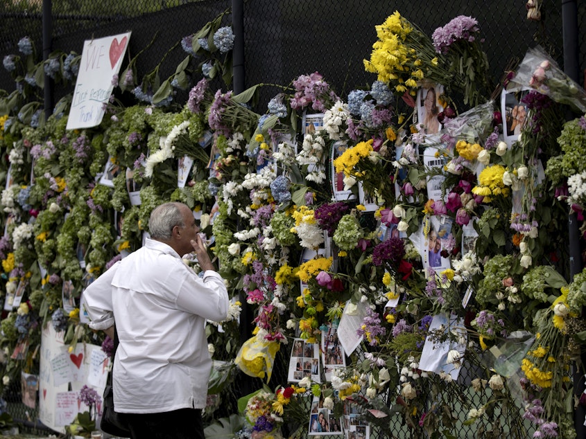 caption: A man looks at a memorial Tuesday with pictures of some of the missing from the partially collapsed 12-story Champlain Towers South condo building in Surfside, Fla.